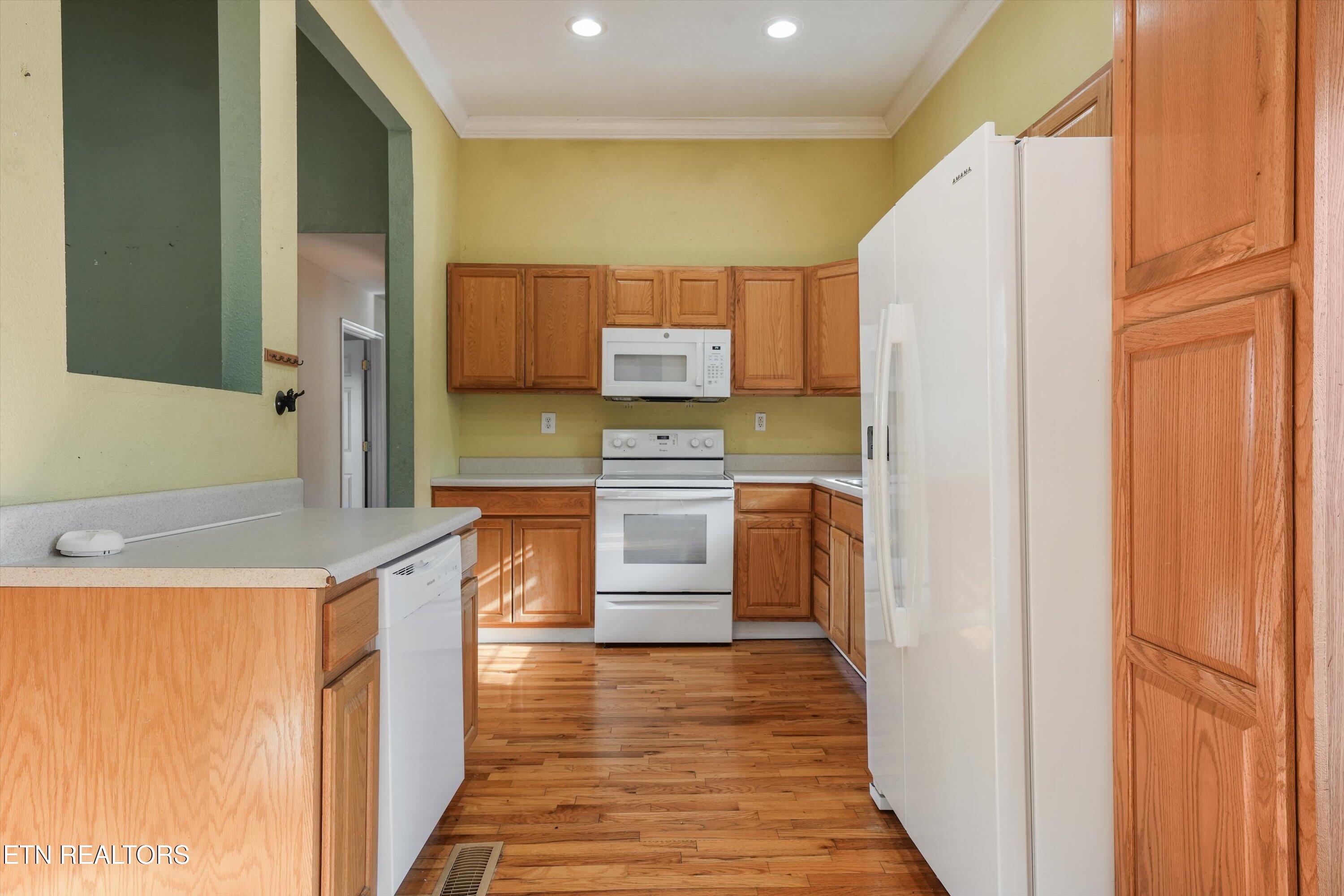 Kitchen with honey-toned wood cabinets, white appliances, hardwood floors, and a broad peninsula counter.