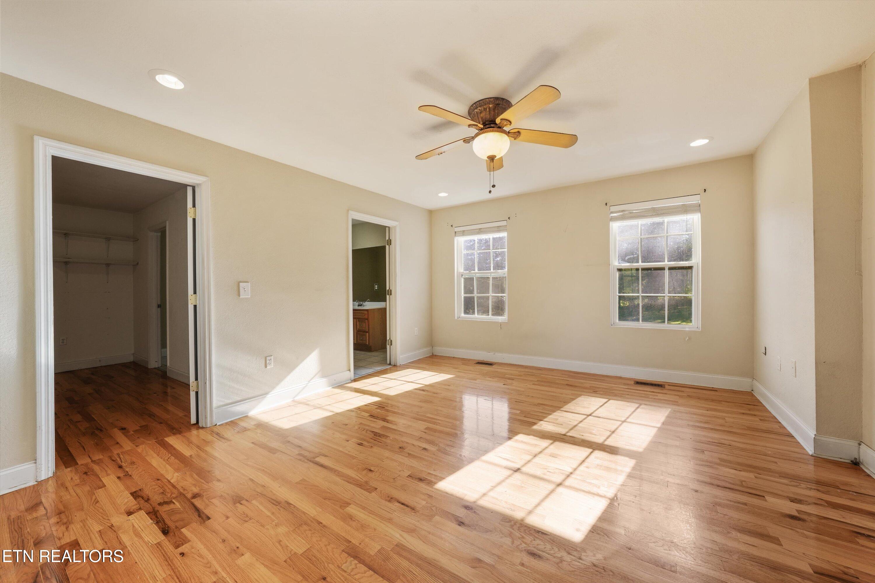 Vacant bedroom with hardwood floors, two sunlit windows, and a ceiling fan.