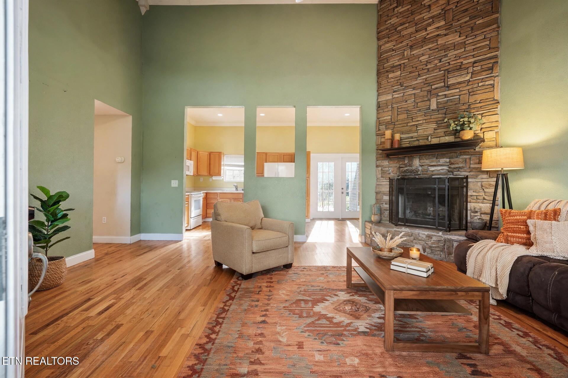 Living room with a tall stone fireplace, sage-green walls, and hardwood floors.