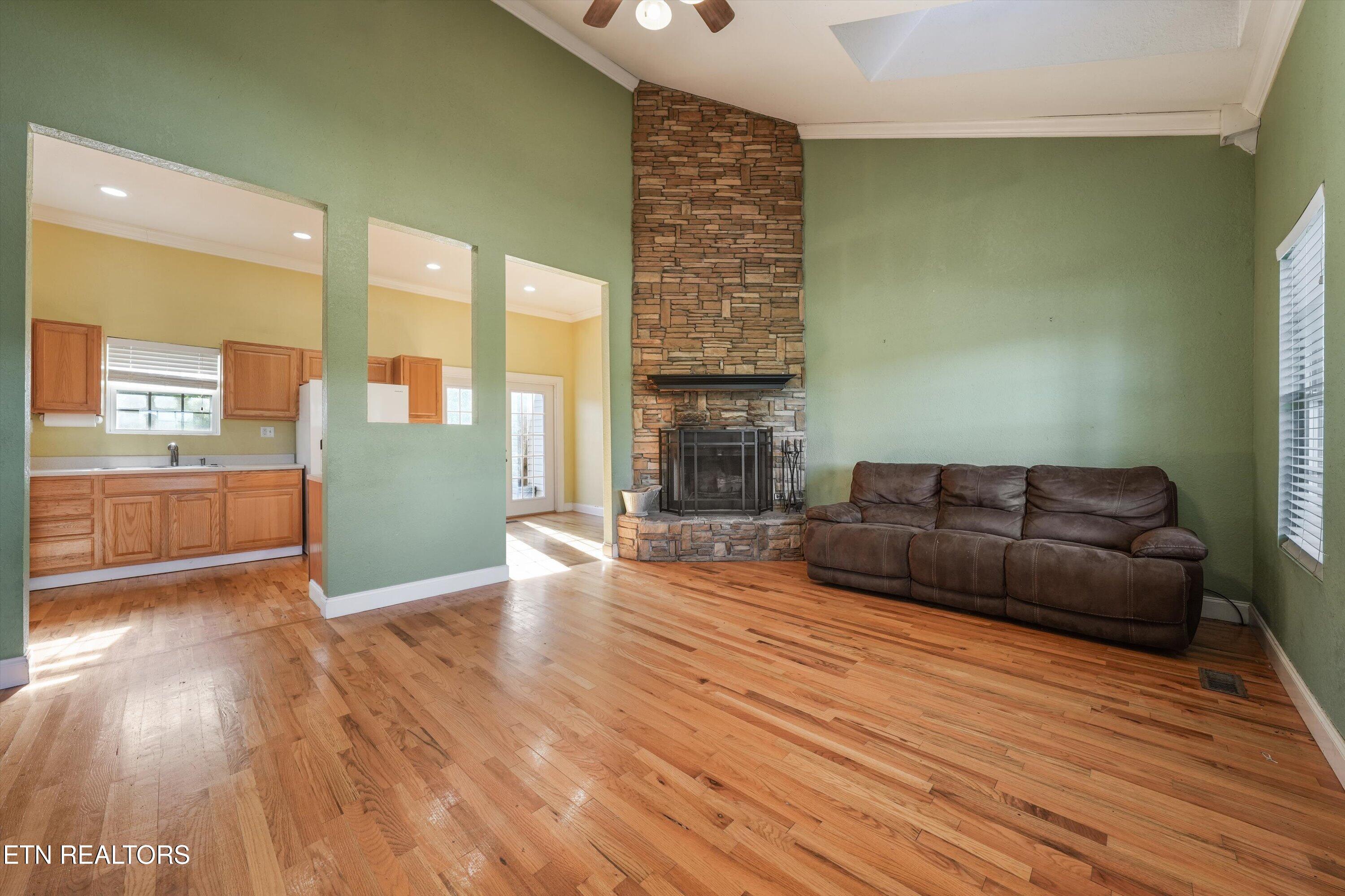 Living room with hardwood floors, a tall stone fireplace, and a brown leather sofa.