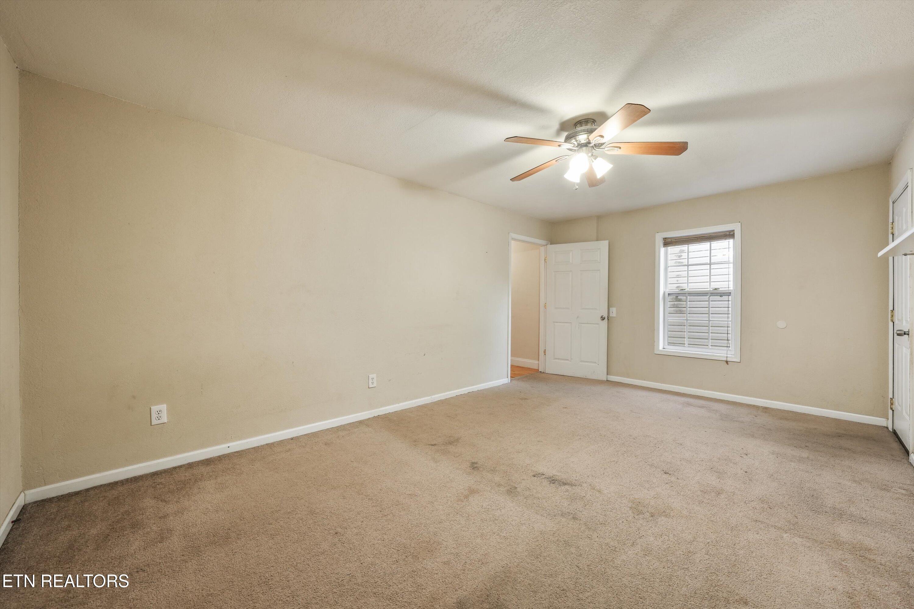 Empty carpeted room with a ceiling fan, window, and open doorway.