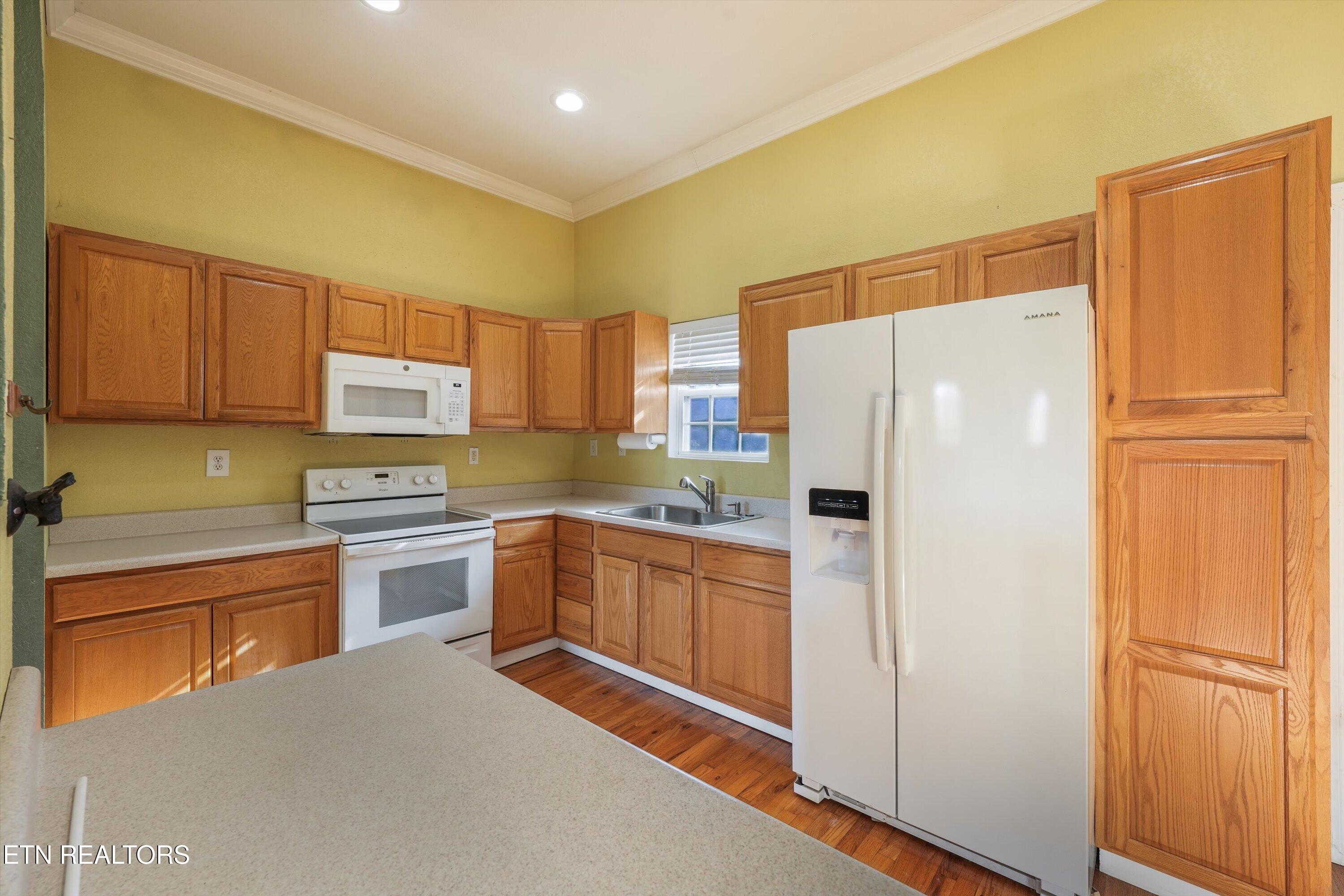 Kitchen with warm wood cabinets, white appliances, light countertops, and hardwood flooring.