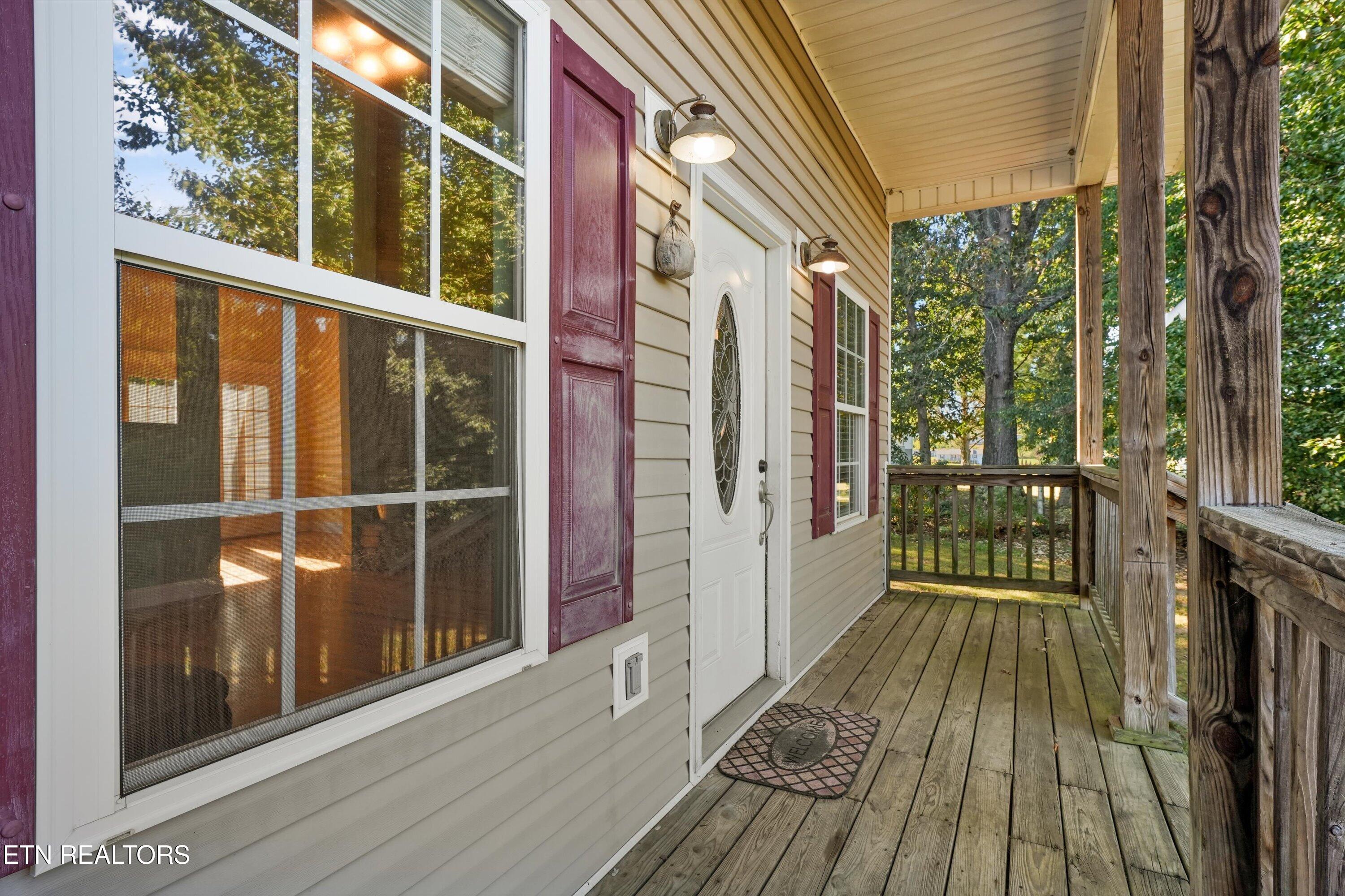 Covered wooden porch with a white entry door, burgundy shutters, and rustic timber railings.