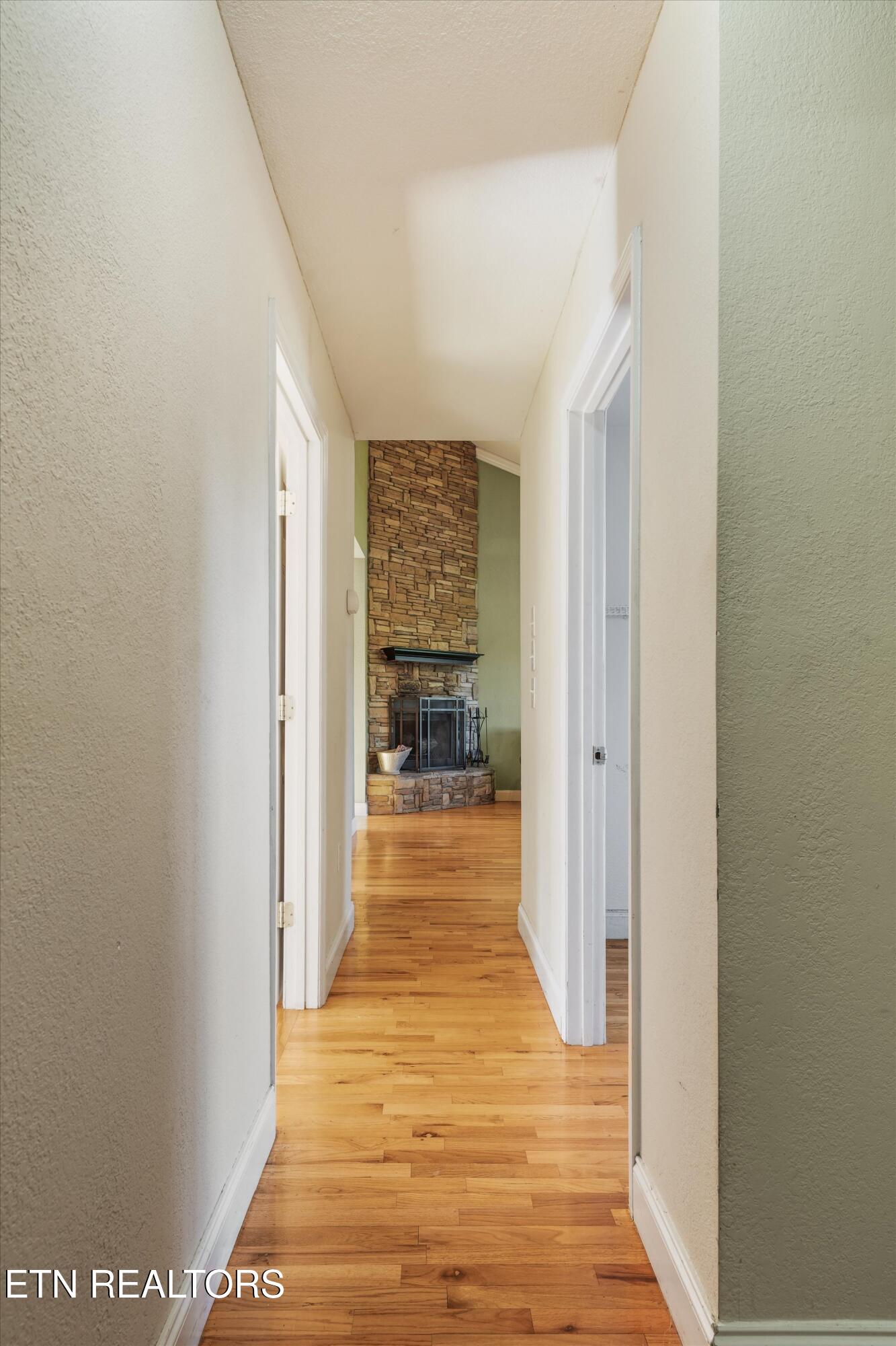 Hallway with hardwood floors leading to a tall stone fireplace.