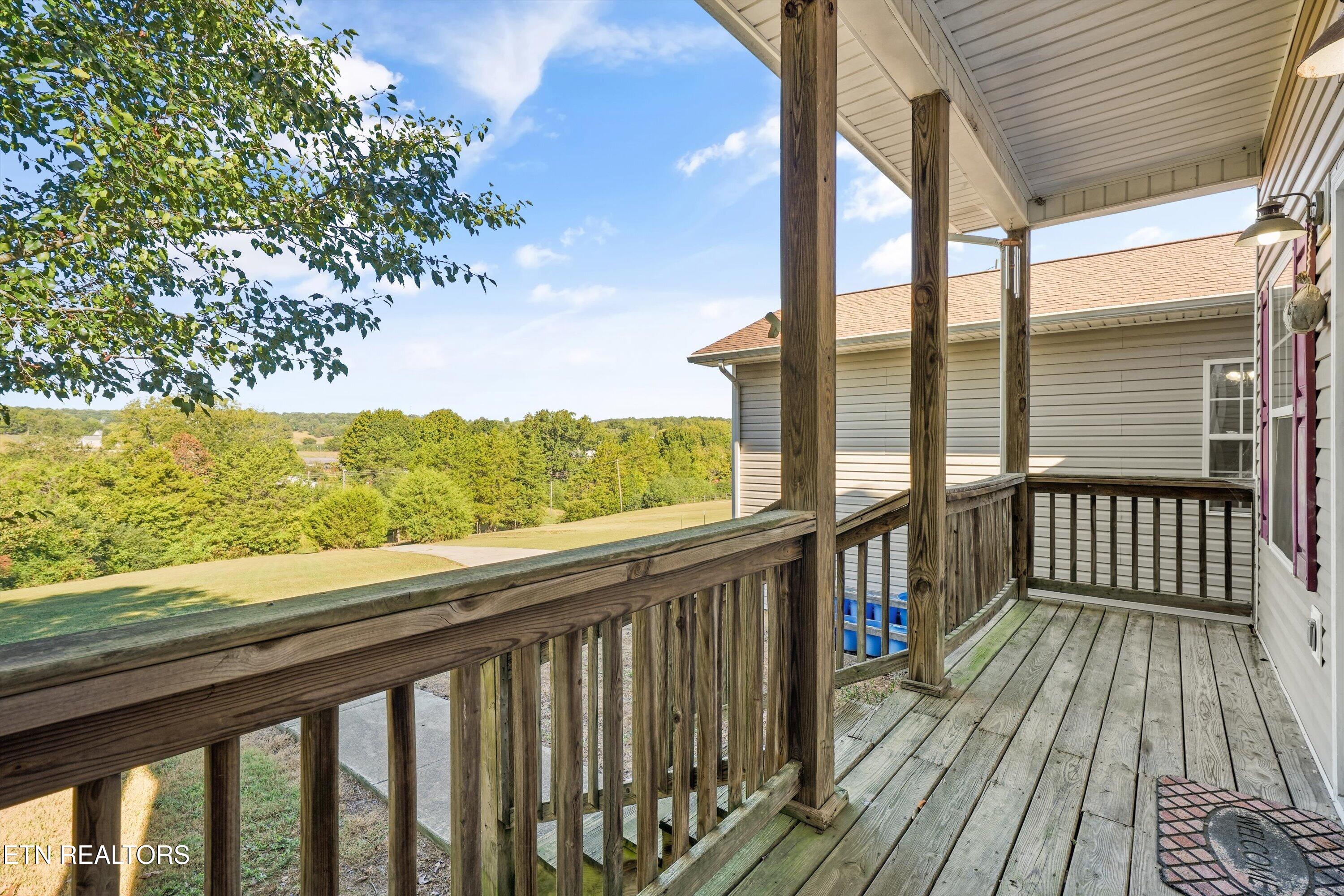 Covered wooden deck overlooking a grassy slope and tree-lined rural landscape.