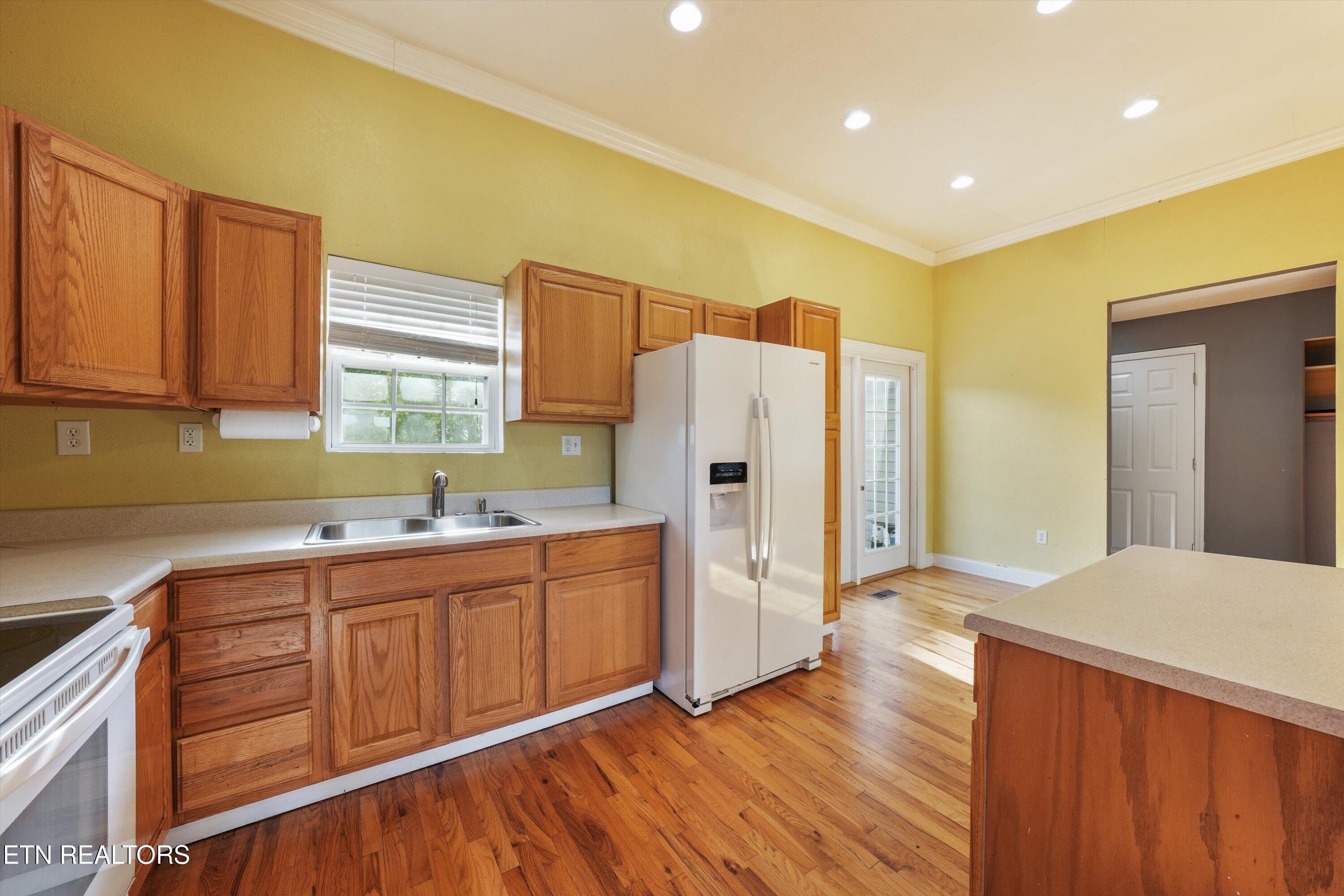 Kitchen with wood cabinets, hardwood floors, and a white refrigerator beside a glass-paneled door.