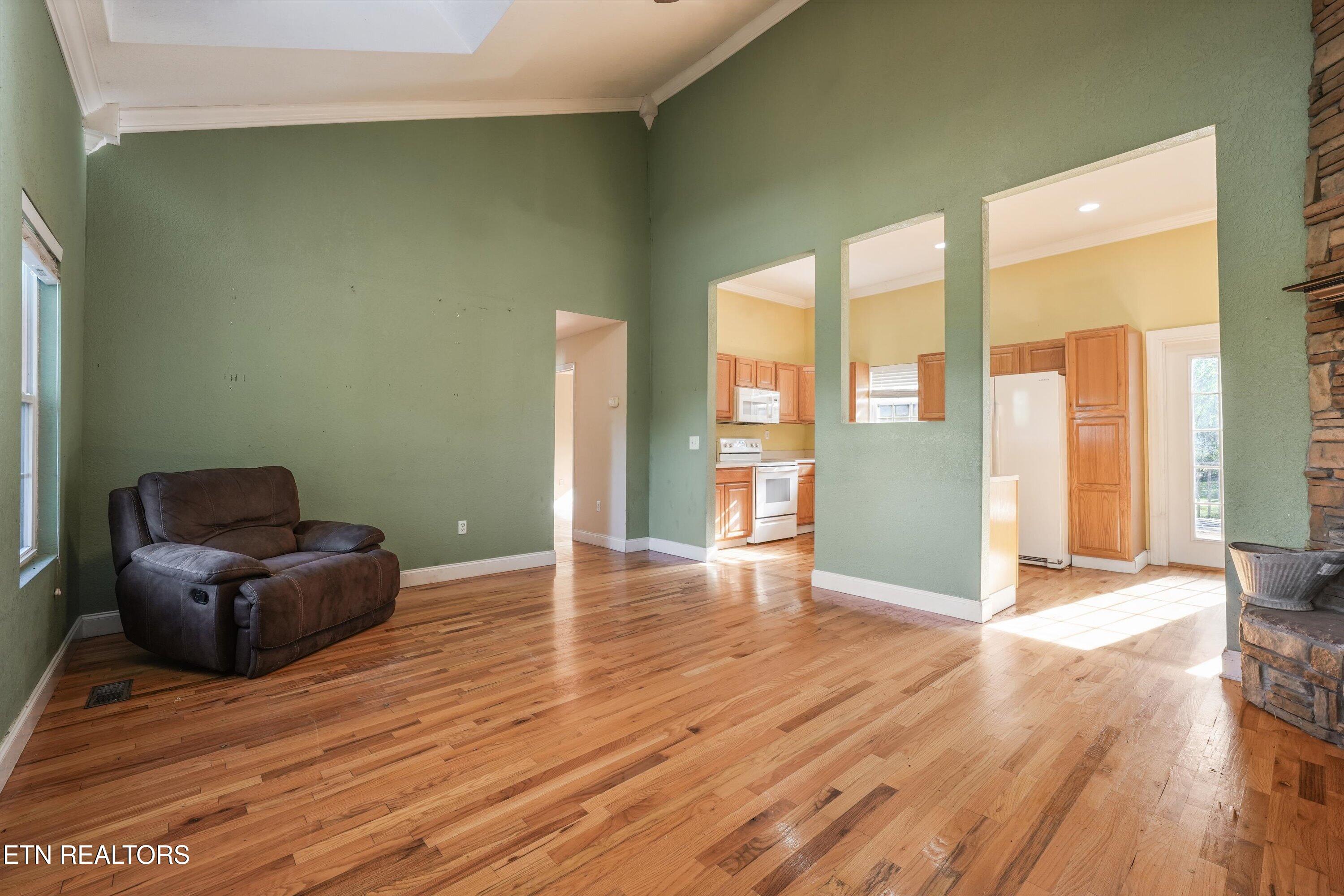 Living room with green walls, hardwood floors, a leather recliner, and openings to the kitchen.