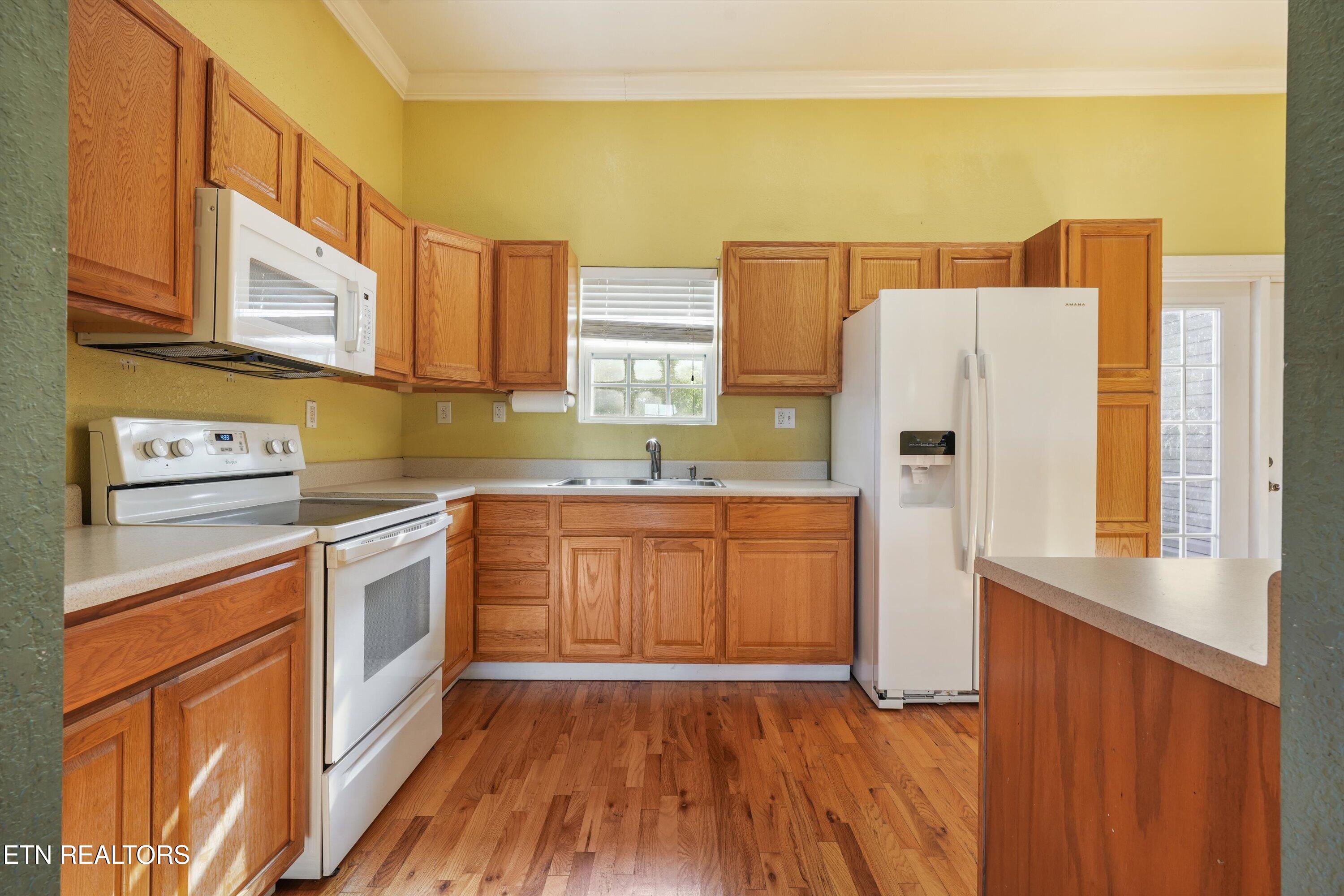 Kitchen with wood cabinets, white appliances, and hardwood floors.