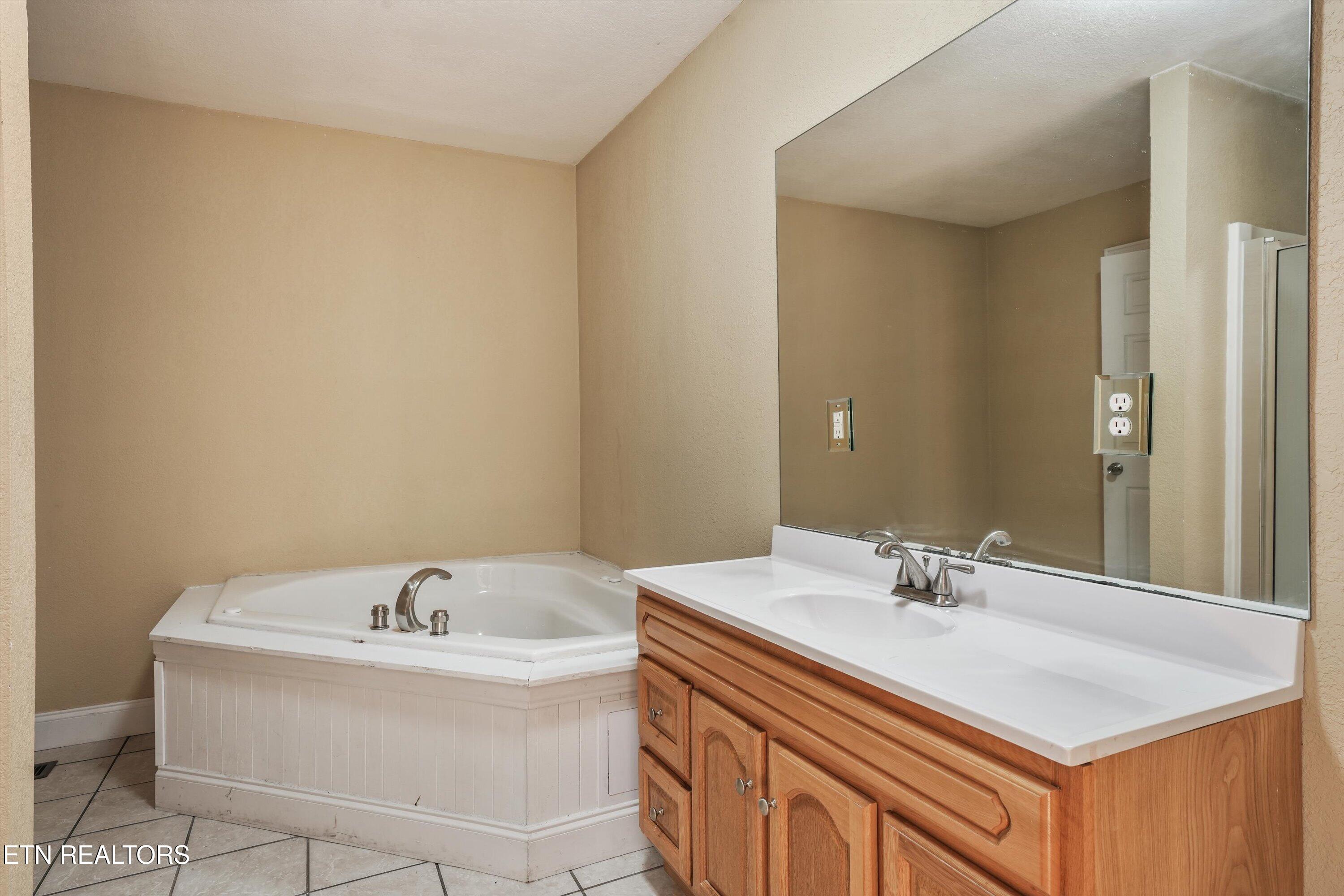 Bathroom with a corner soaking tub, wood vanity, and large mirror.