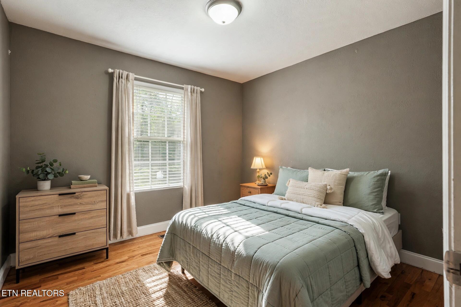 Bedroom with sage bedding, a curtained window, and a wooden dresser.