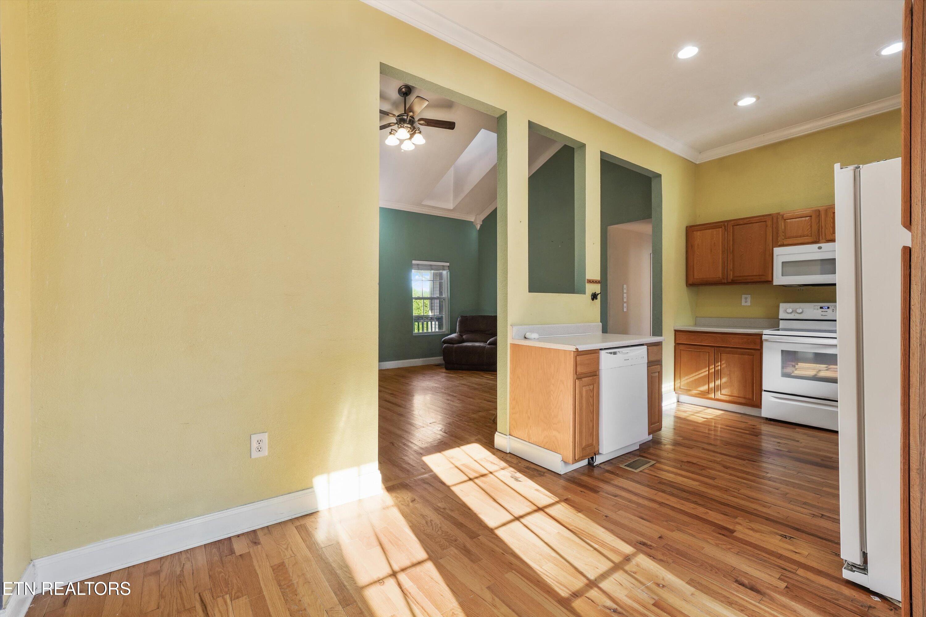 Kitchen with wood cabinets and hardwood floors, opening to a living area with green walls.