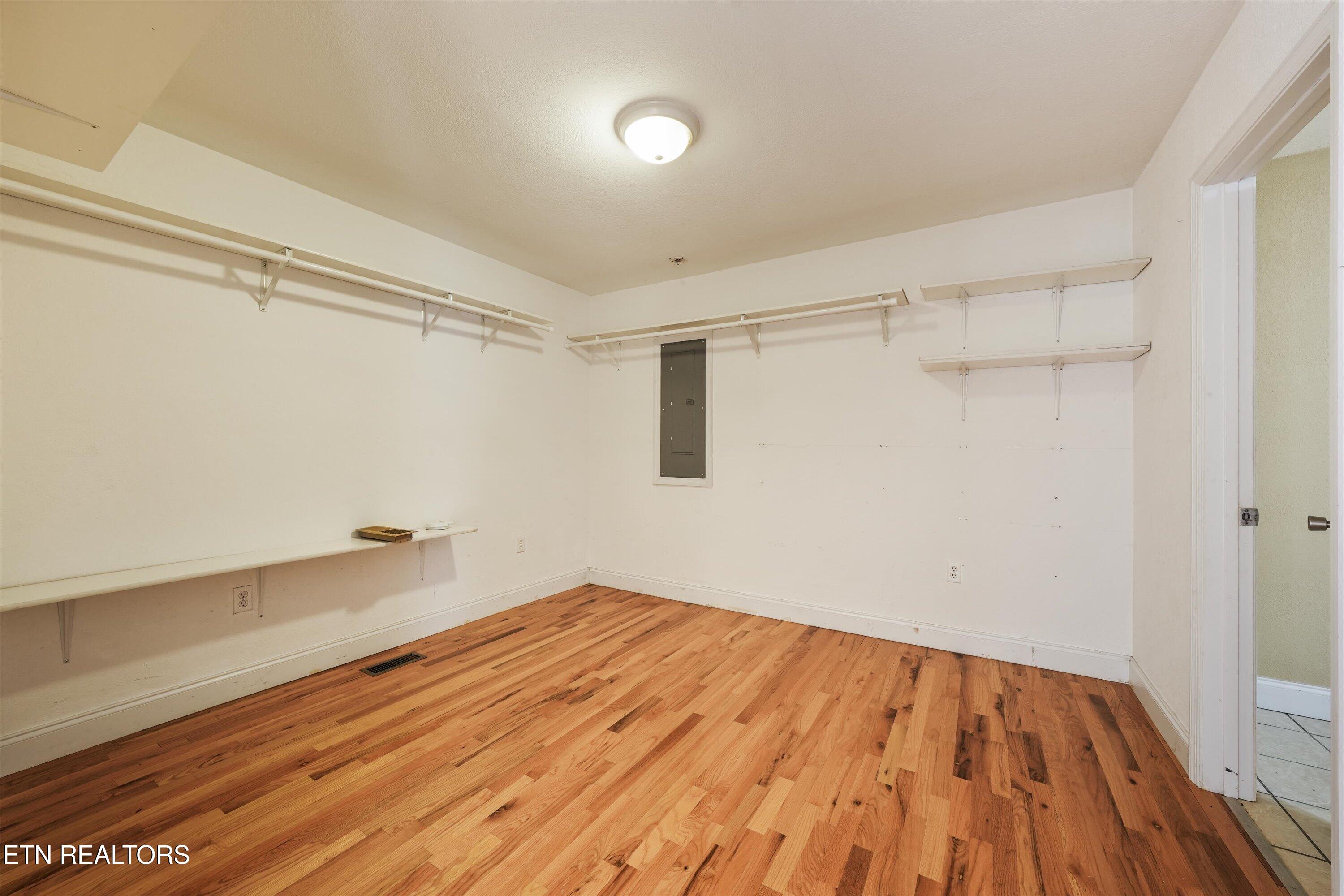 Walk-in closet with built-in shelves and hanging rails, hardwood floors, and a doorway to a tiled room.