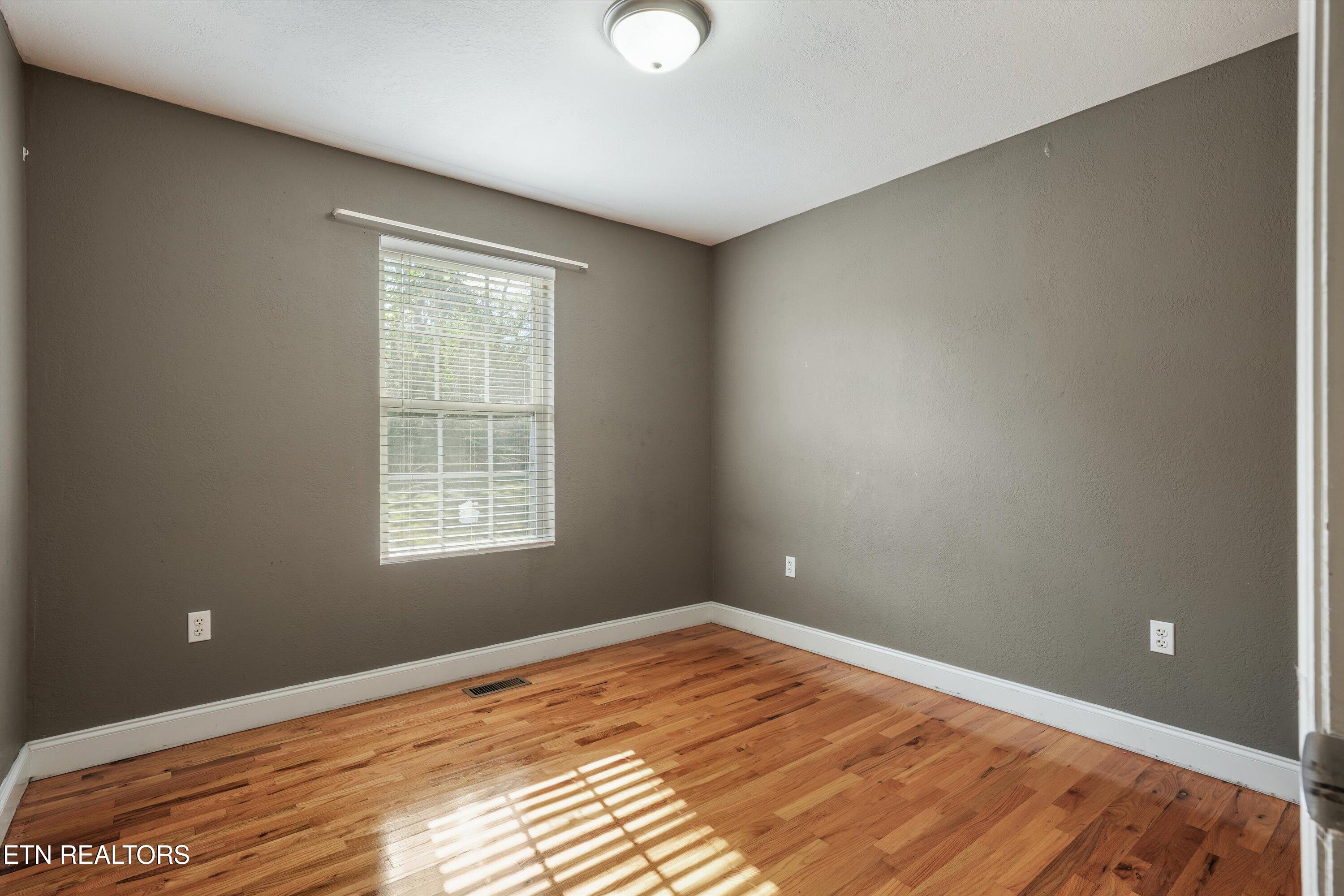 Empty room with hardwood floors, gray walls, and a window with white blinds.