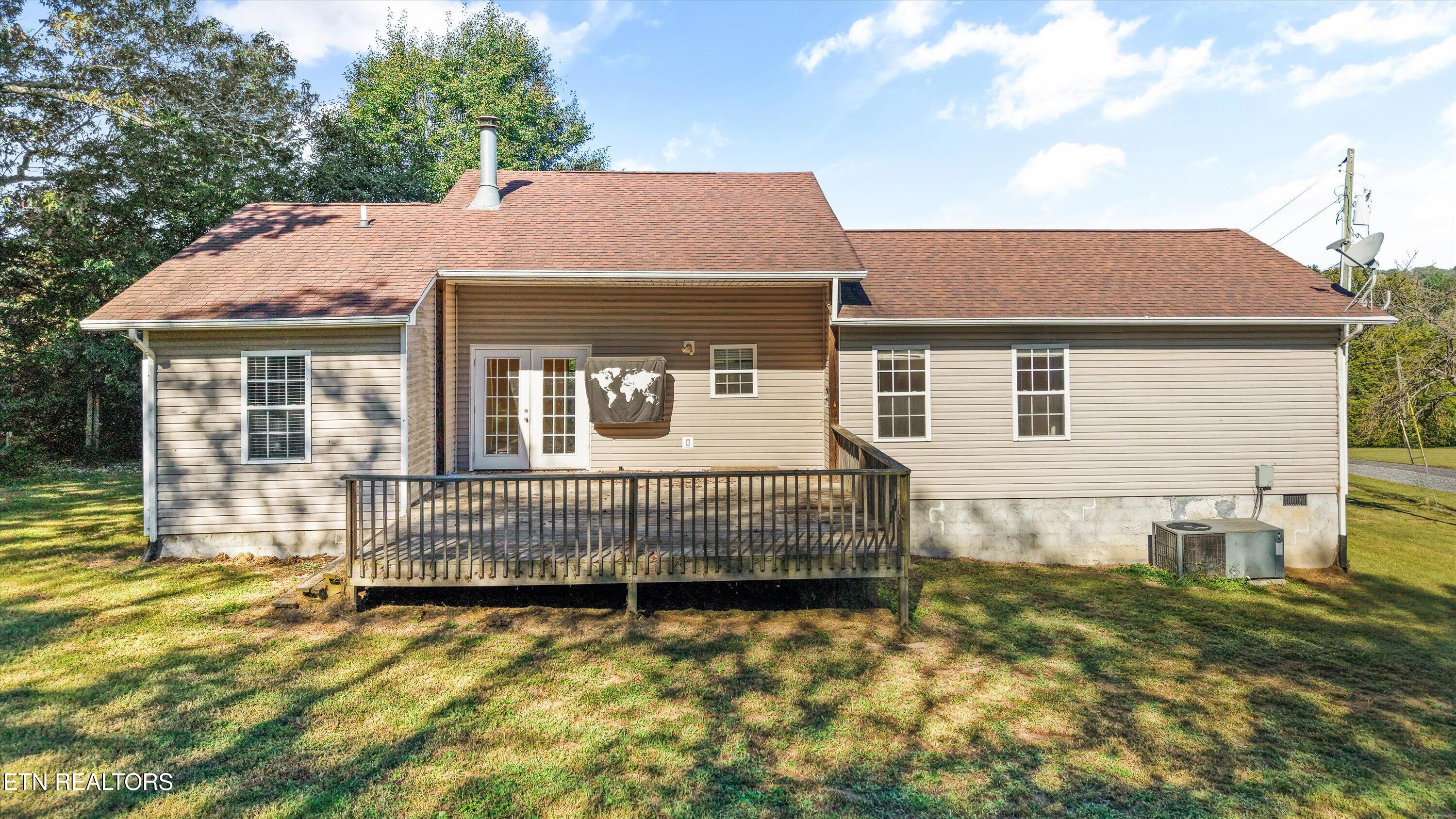 Rear of a beige-sided home with a raised deck, French doors, and a broad shingle roof.