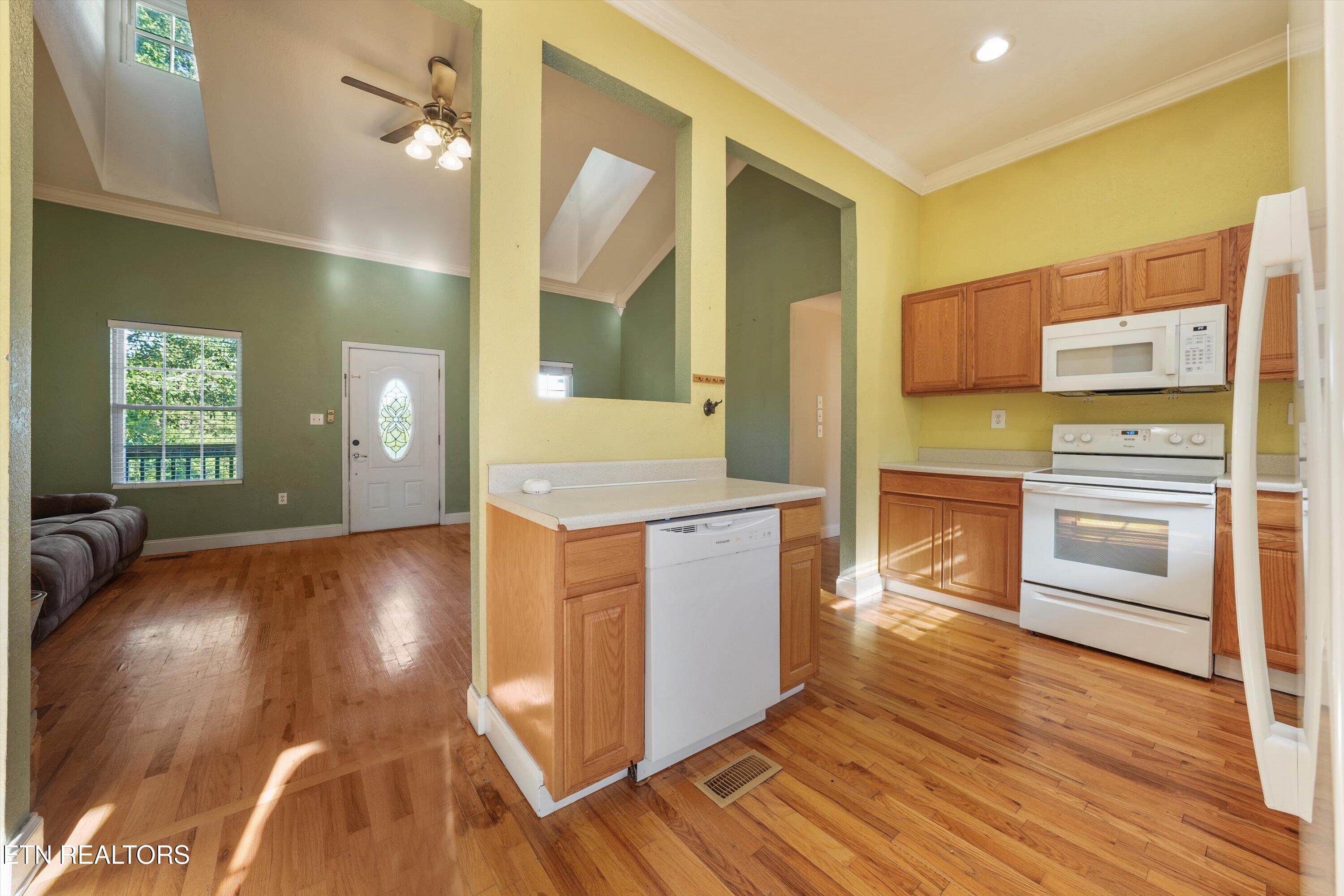Open kitchen and living area with oak cabinets, white appliances, hardwood floors, and vaulted ceilings.