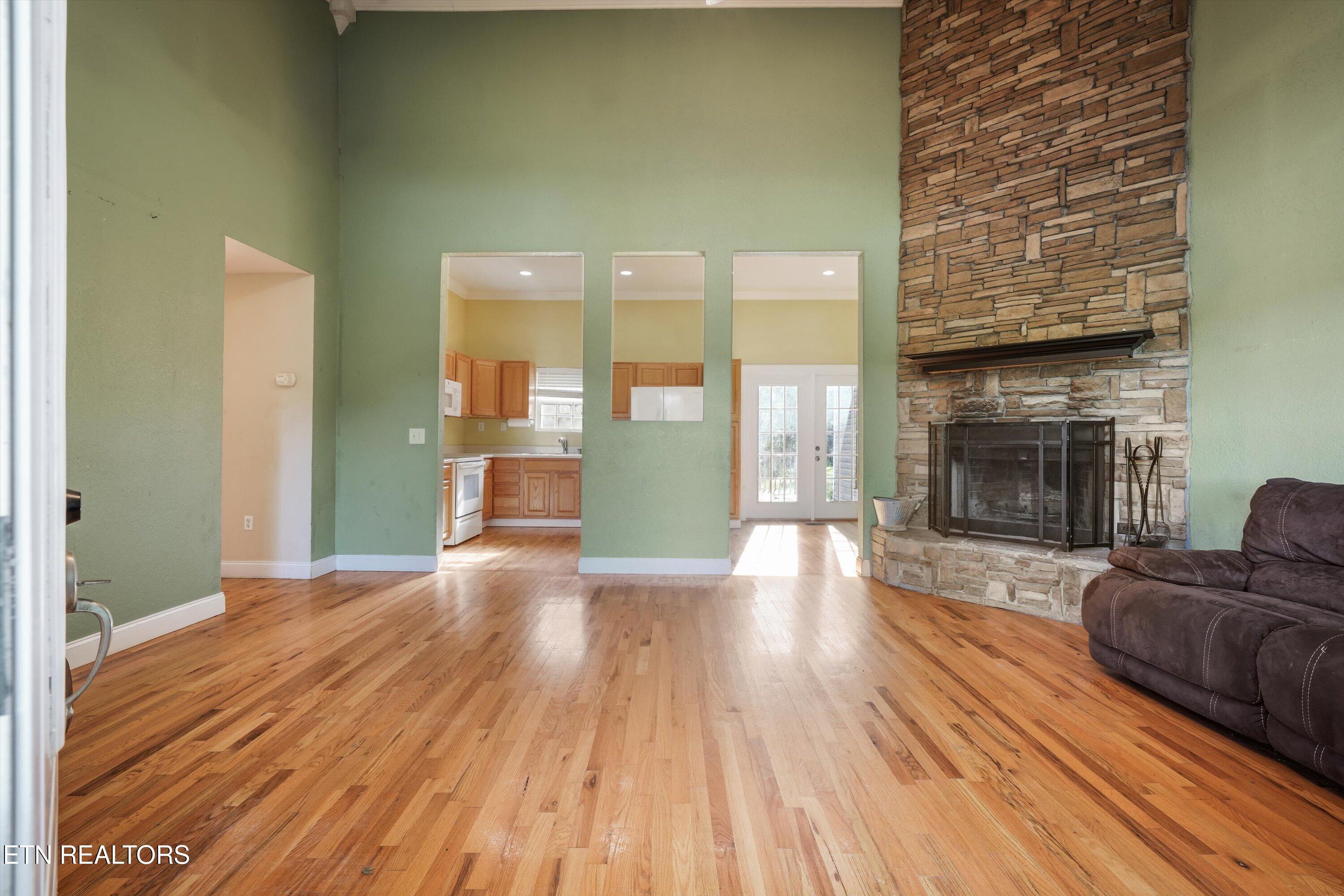 Living room with hardwood floors, a tall stone fireplace, and a view into the kitchen.
