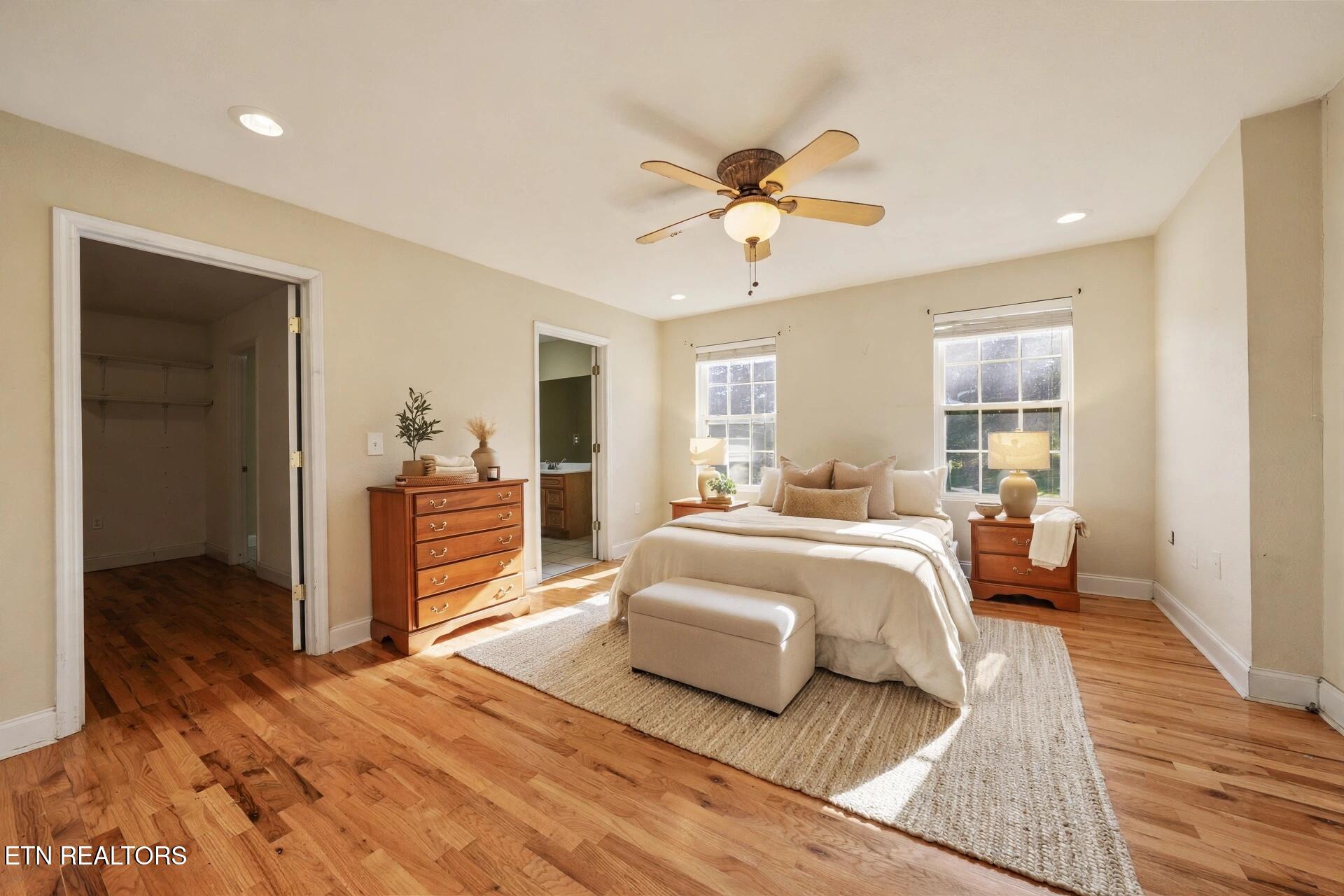 Bedroom with a king-size bed, hardwood floors, ceiling fan, and adjoining bathroom.