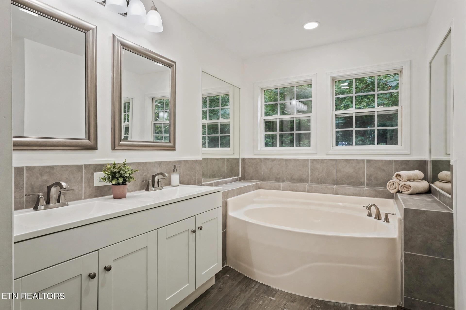 Bright bathroom with a corner soaking tub beneath three windows and a white vanity.