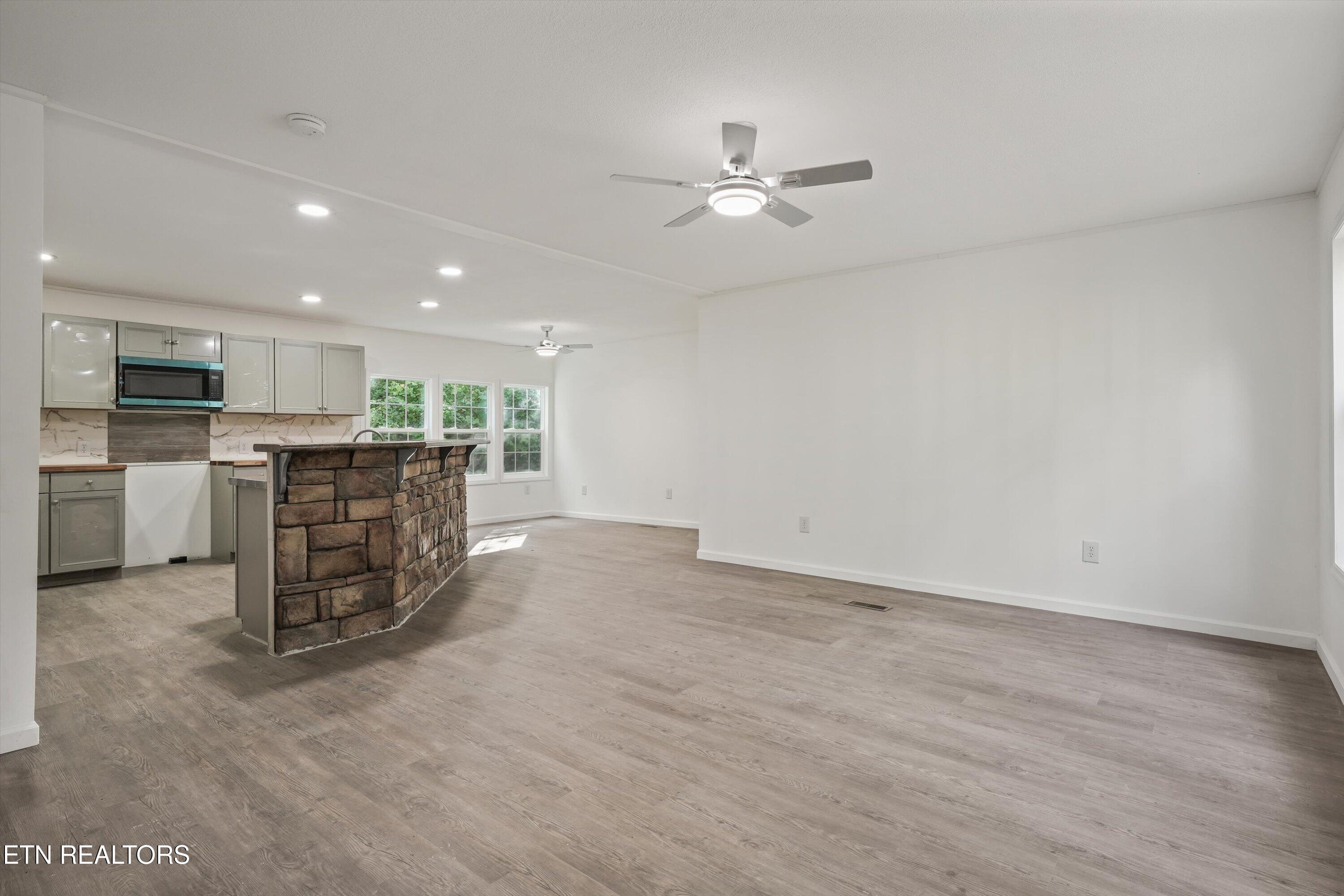 Open kitchen and living area with a stone-front breakfast bar and gray wood-look flooring.
