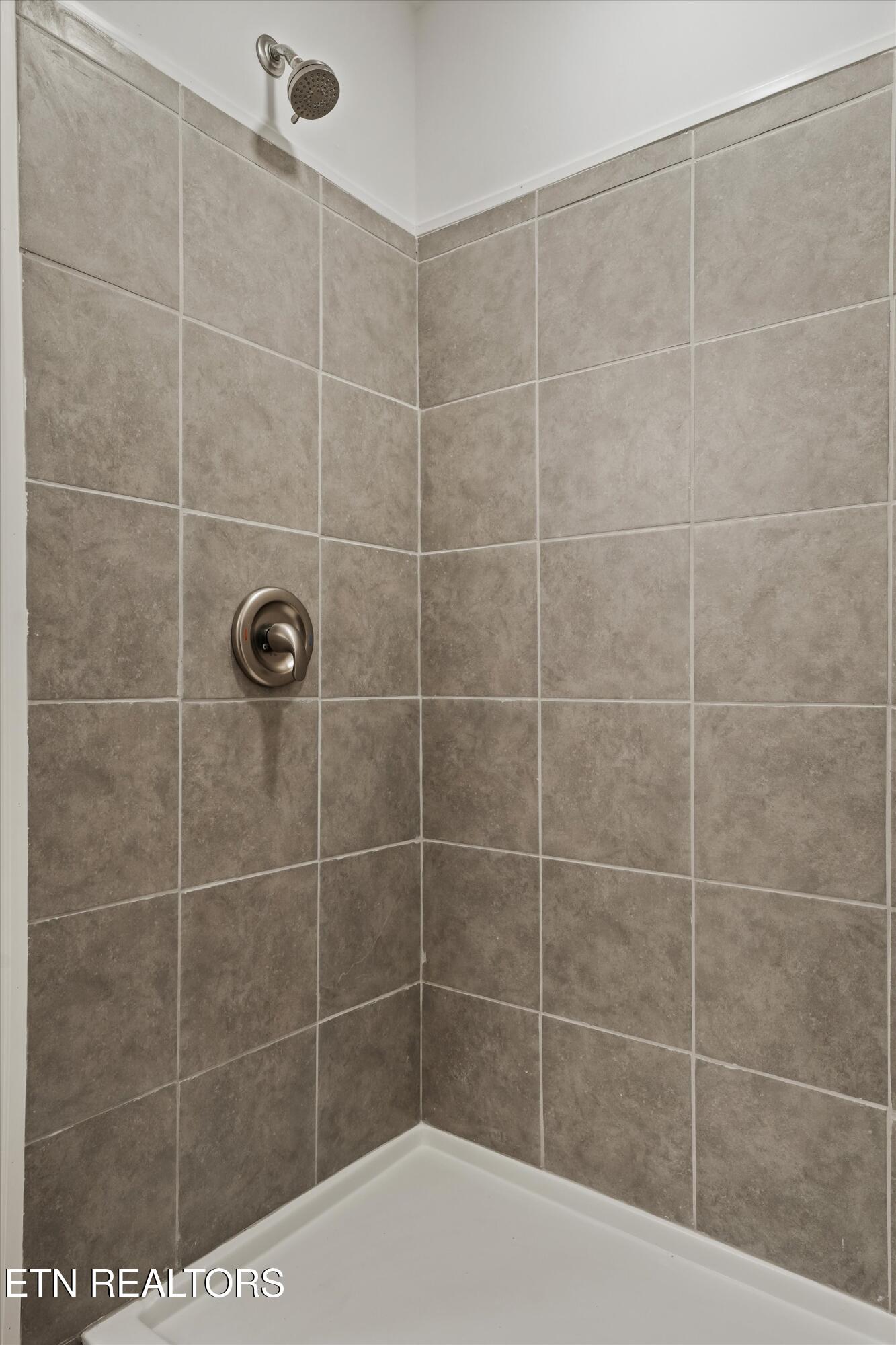 Tiled shower with brushed metal fixtures and a white shower base.
