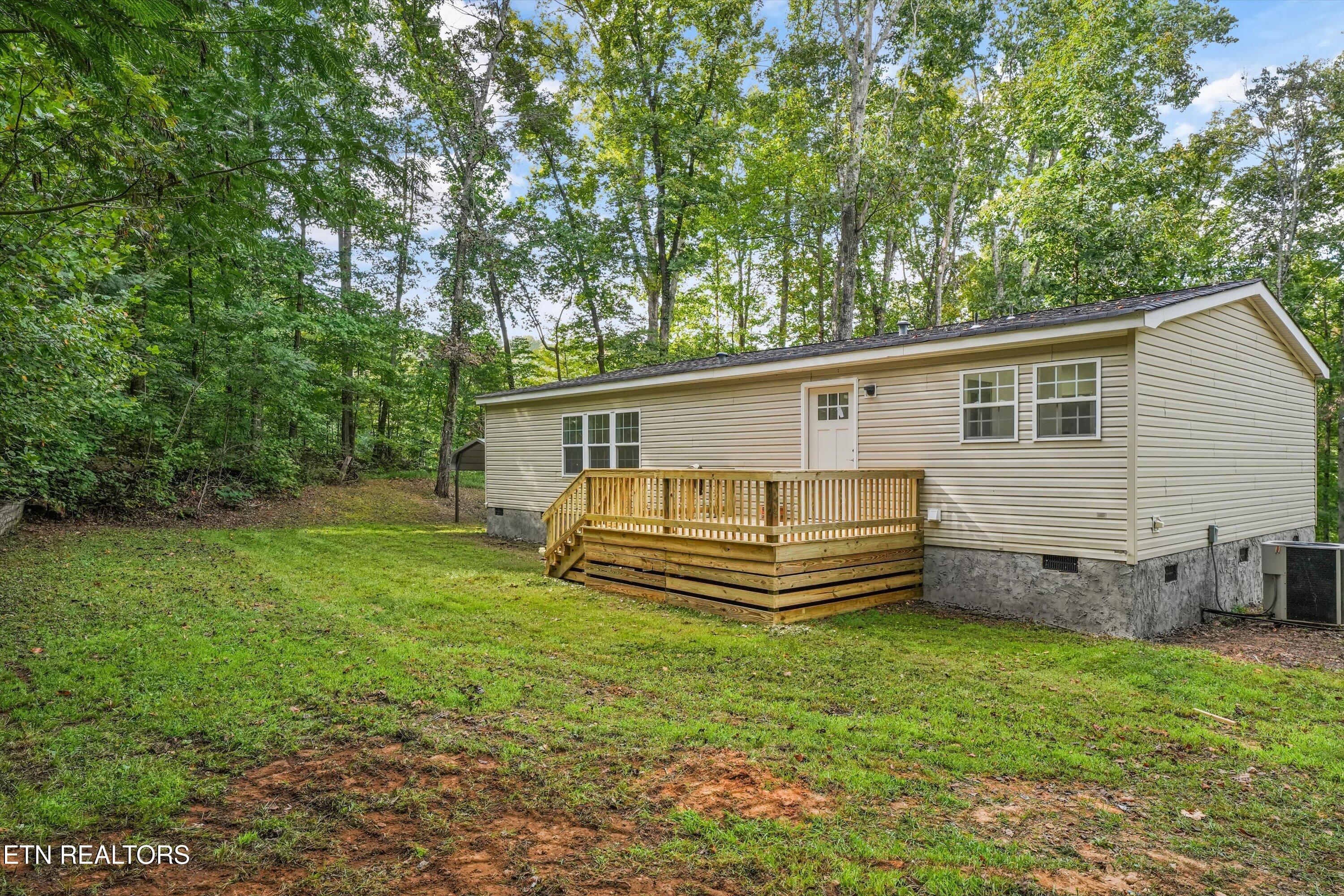 Beige-sided home with a raised wooden deck on a grassy, wooded lot.