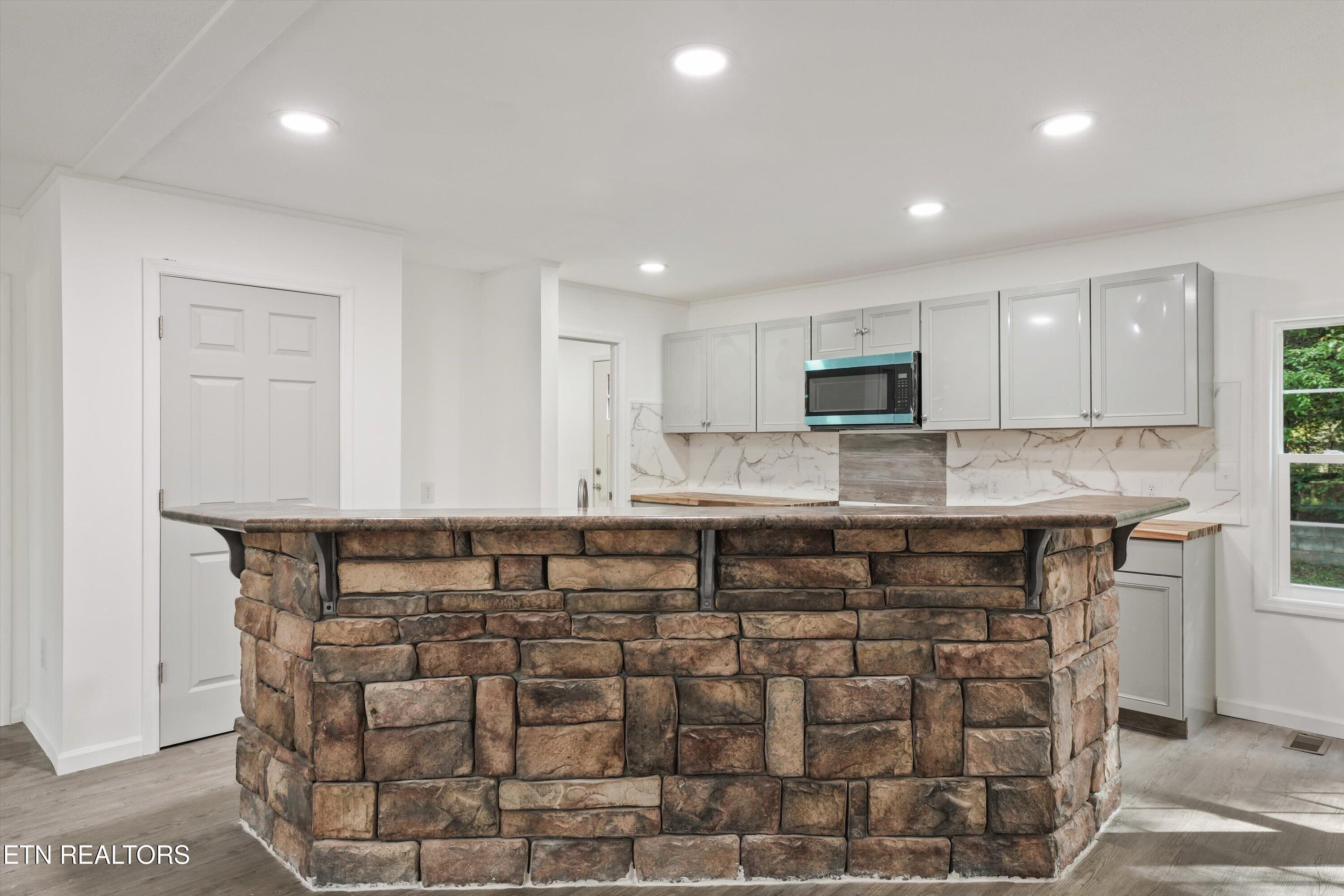 Kitchen with a curved stone-faced island, gray cabinets, and a marble-look backsplash.