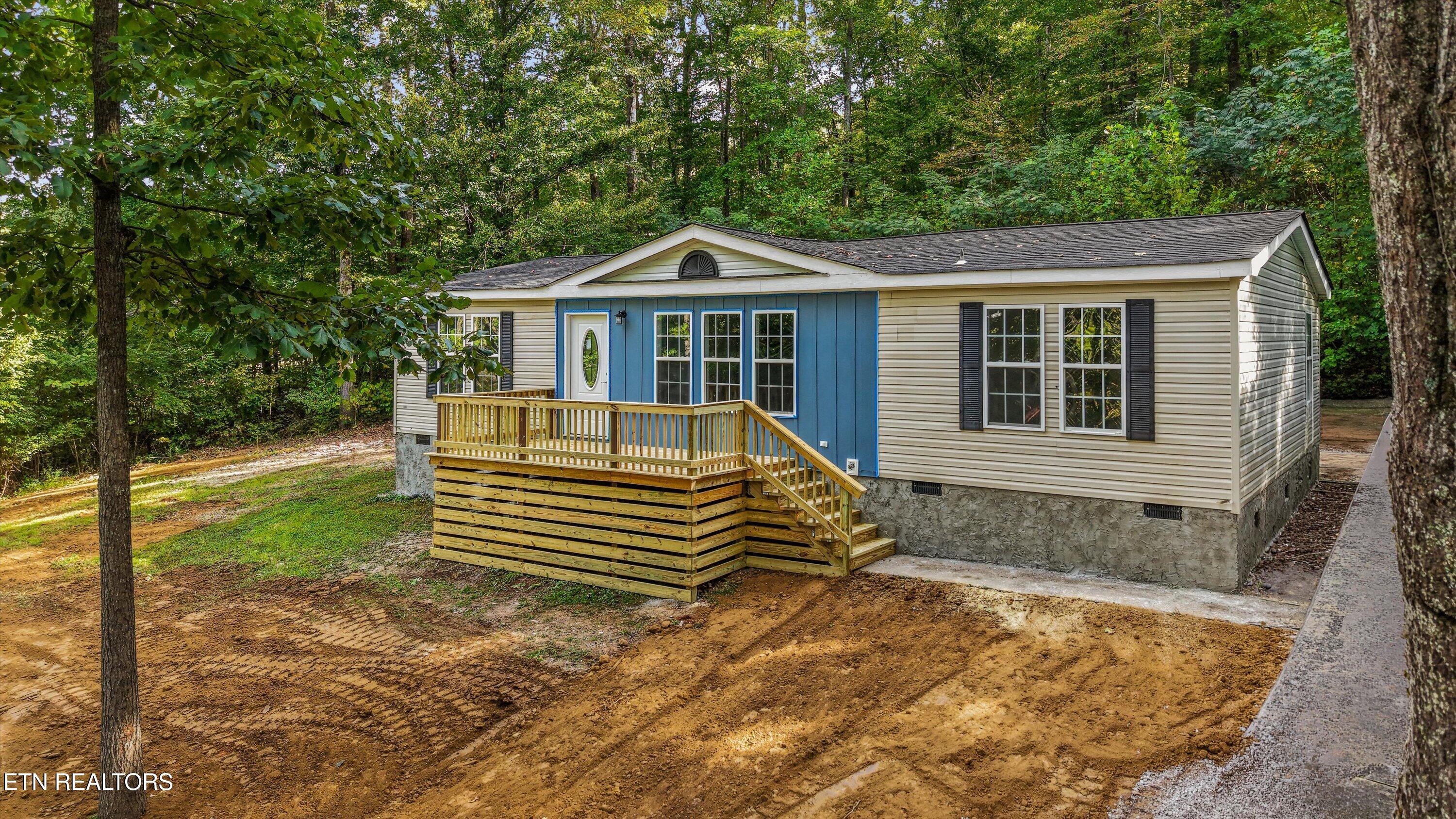 Single-story home with blue entrance facade and raised wooden porch, surrounded by trees.