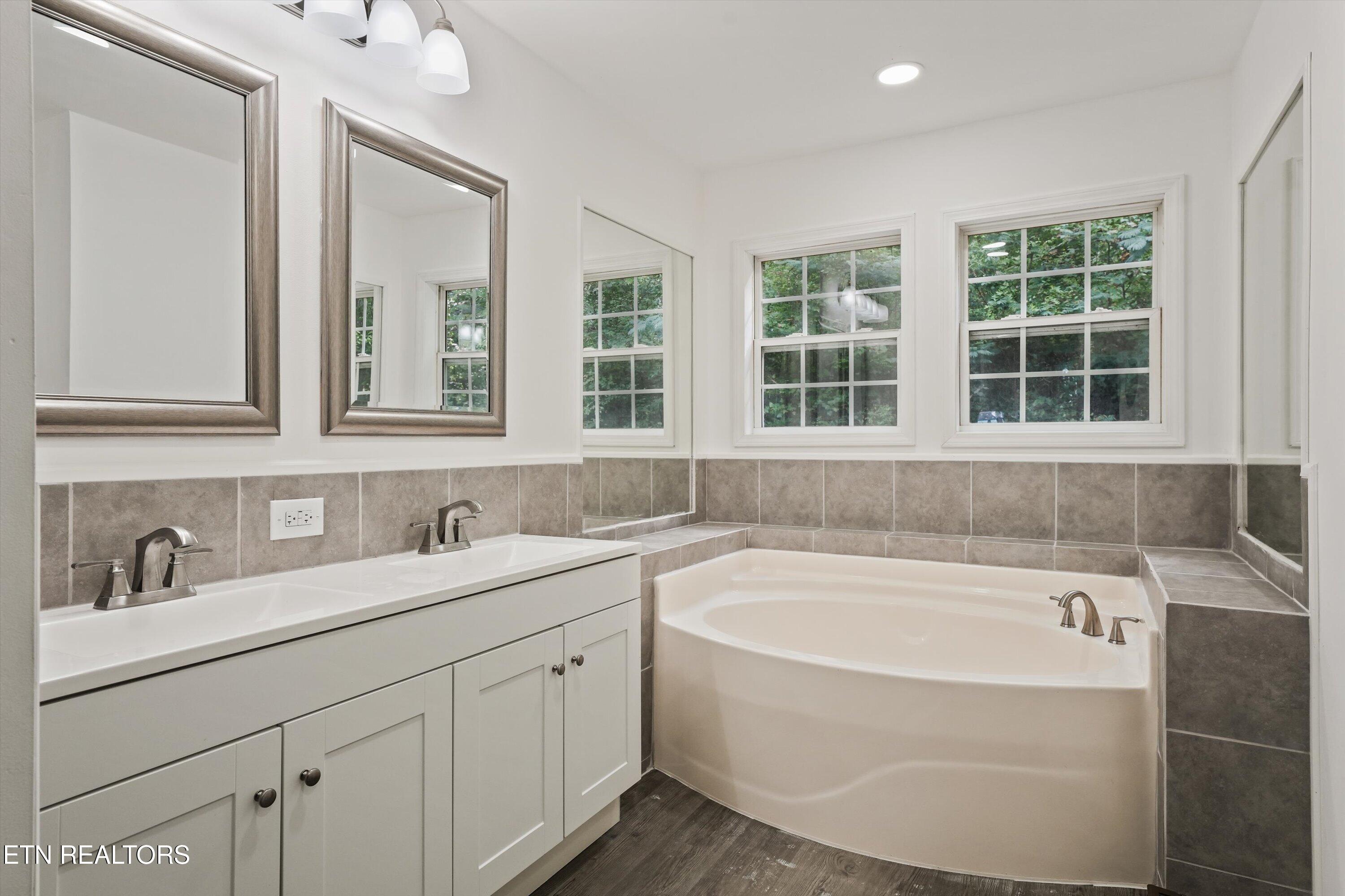 Bathroom with a double vanity and large corner soaking tub beneath three windows.
