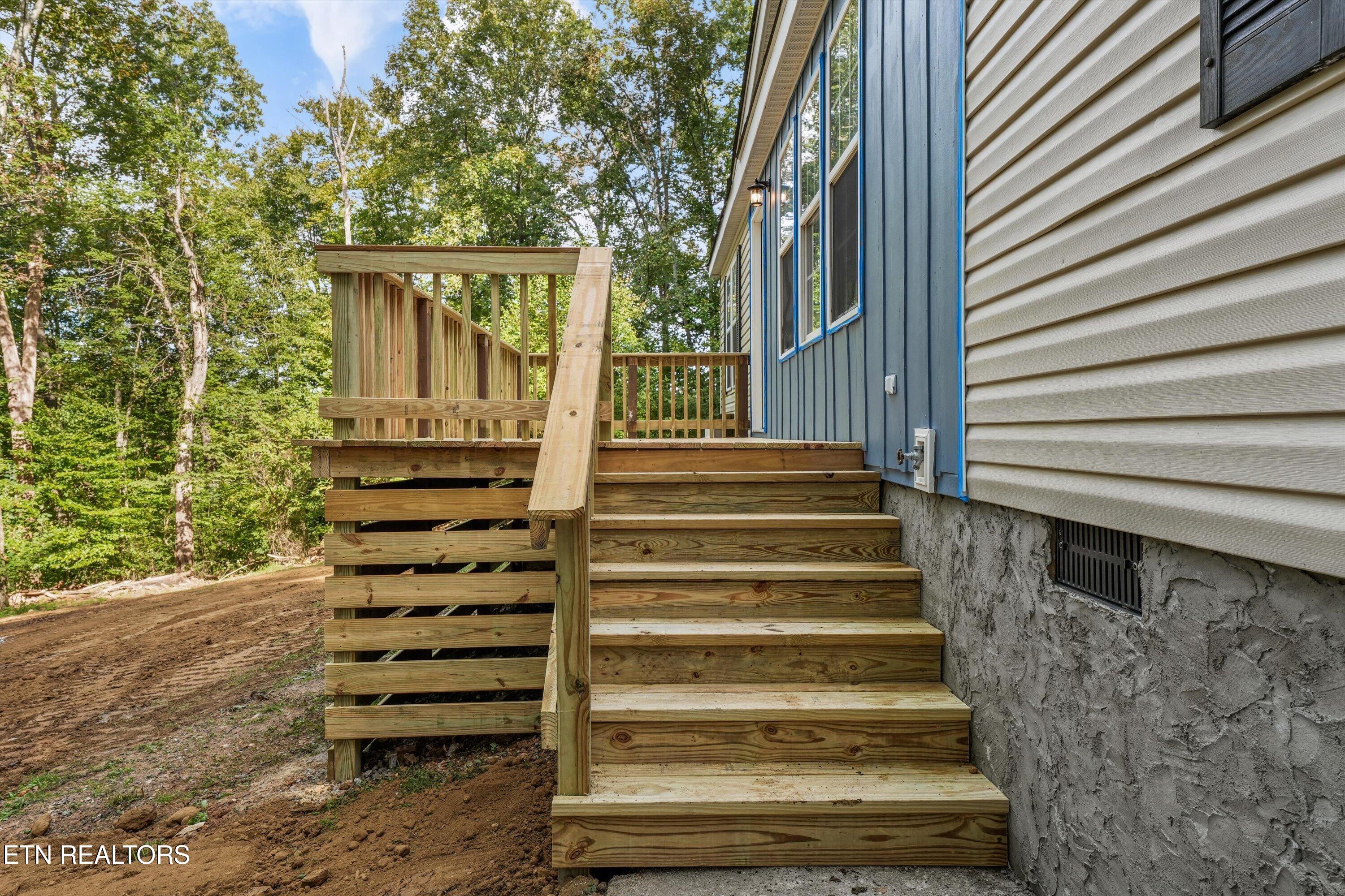 Wooden stairs and raised deck beside a blue-and-white house in a wooded yard