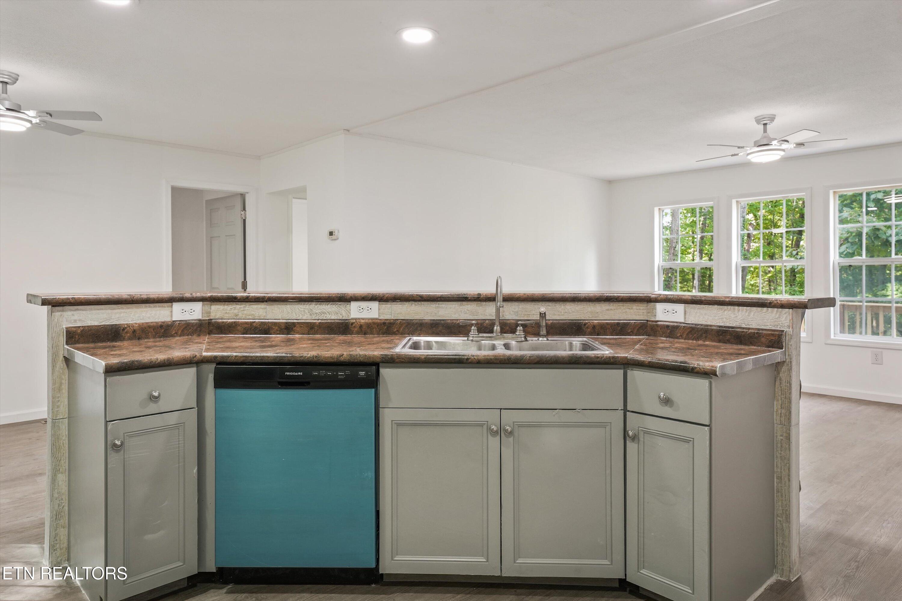Kitchen peninsula with brown patterned counters, gray cabinets, a double sink, and a teal-front dishwasher.