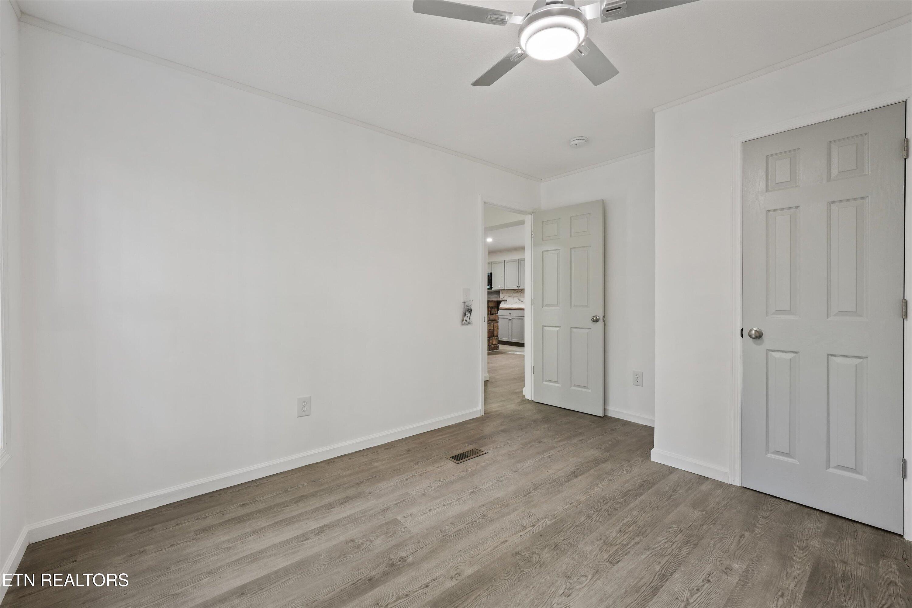 Empty room with wood-look flooring, a ceiling fan, and an open doorway to the kitchen.