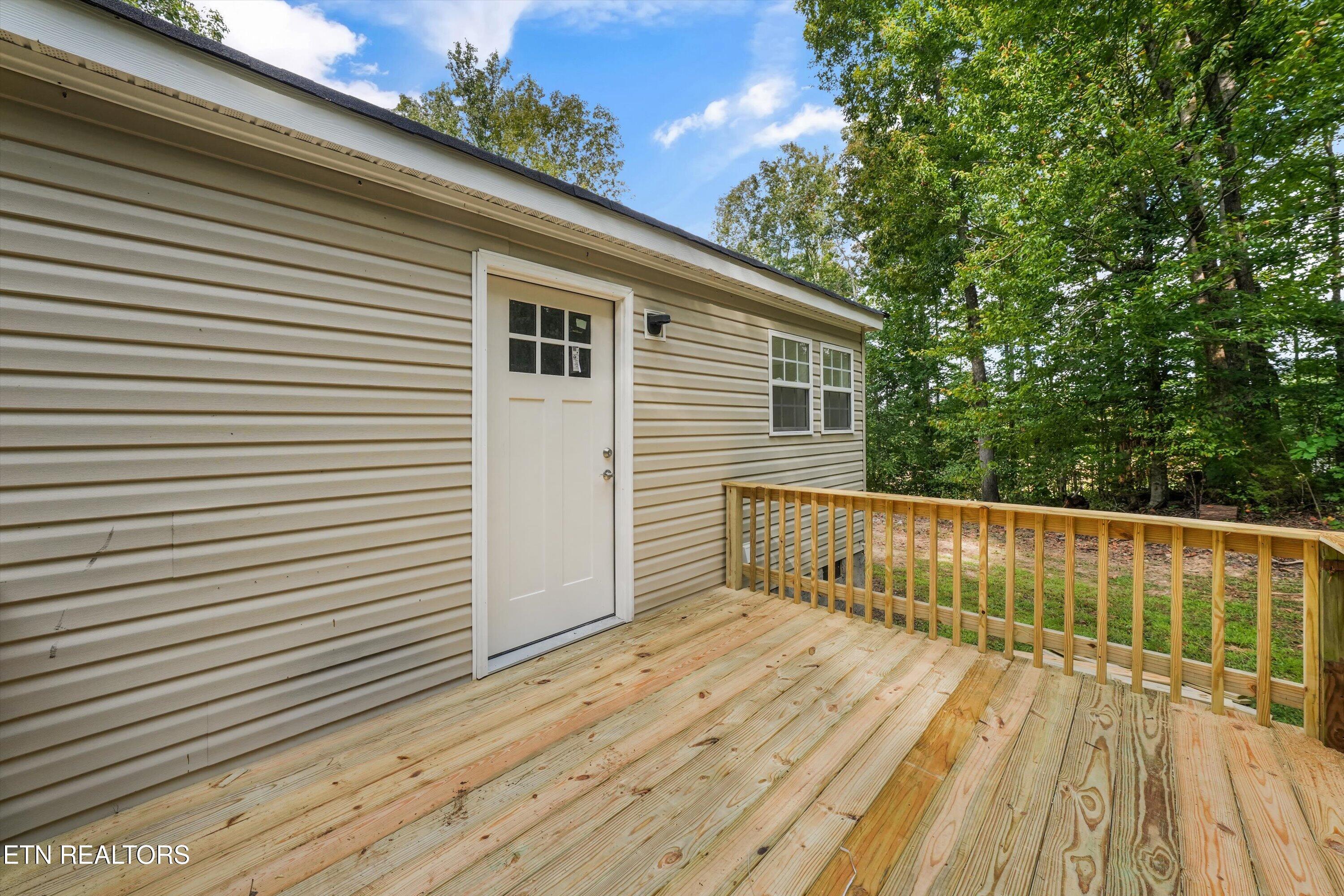 Home’s beige-sided exterior and white door beside a spacious wooden deck overlooking trees.