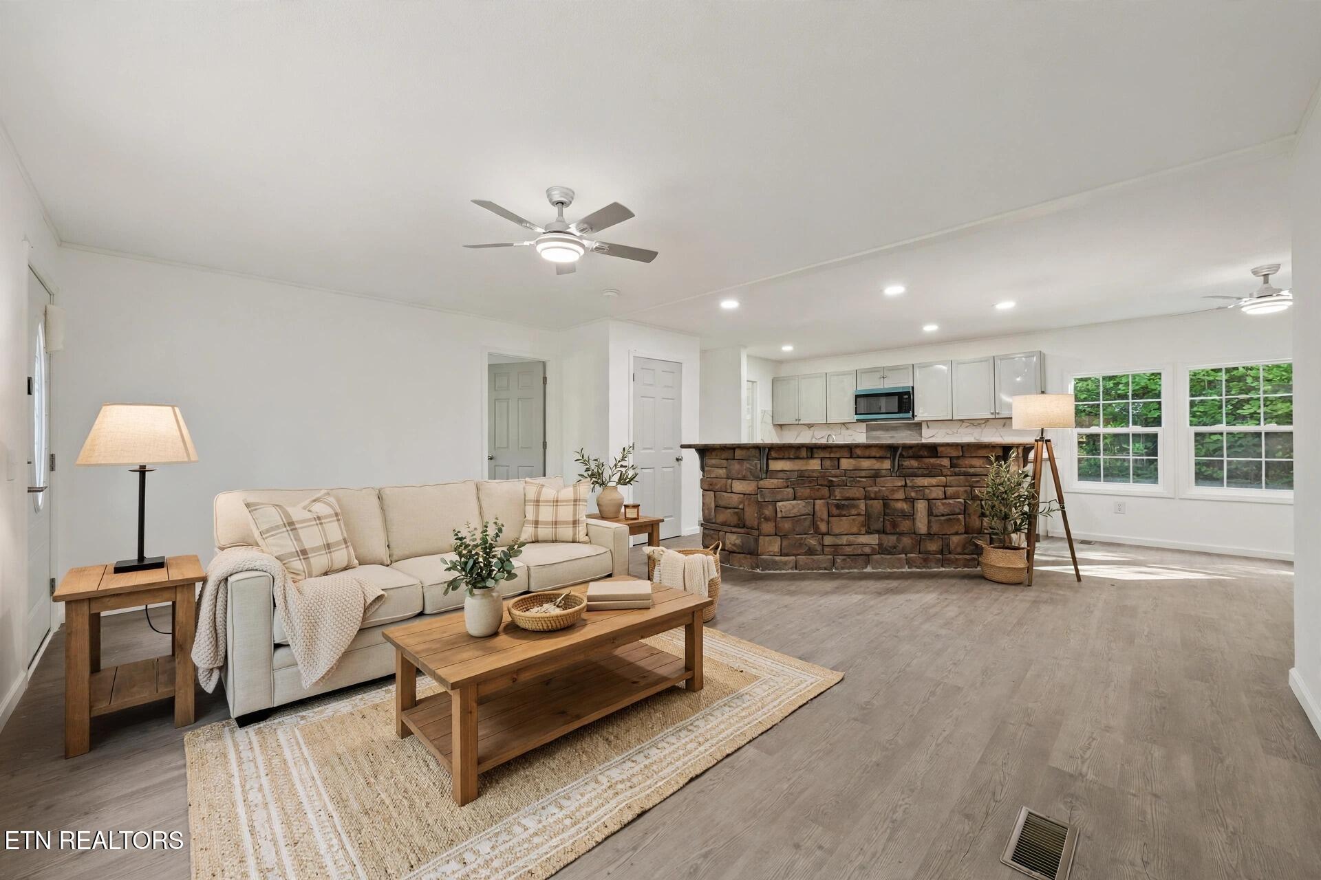 Staged living room with a stone breakfast bar, light sofa, and windows overlooking greenery.