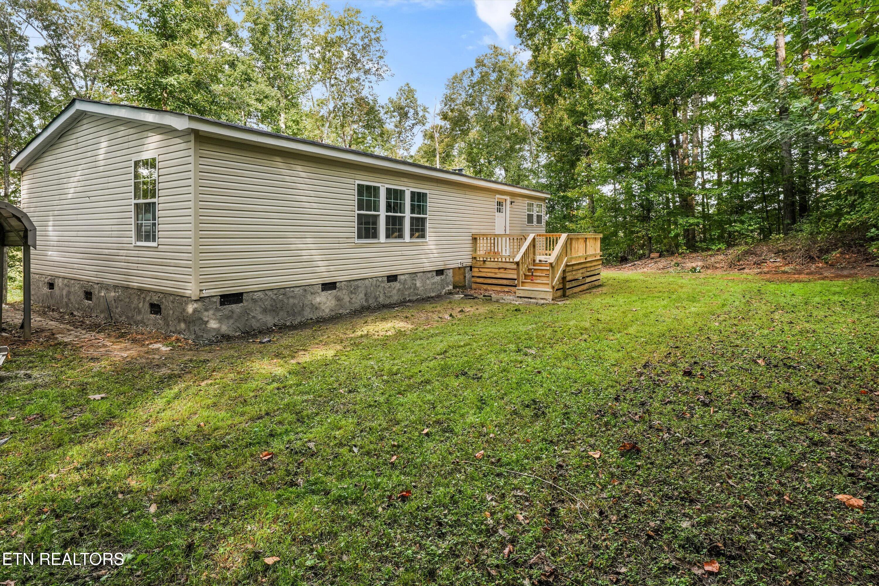 Beige-sided home with a raised wooden deck beside a grassy, wooded yard.