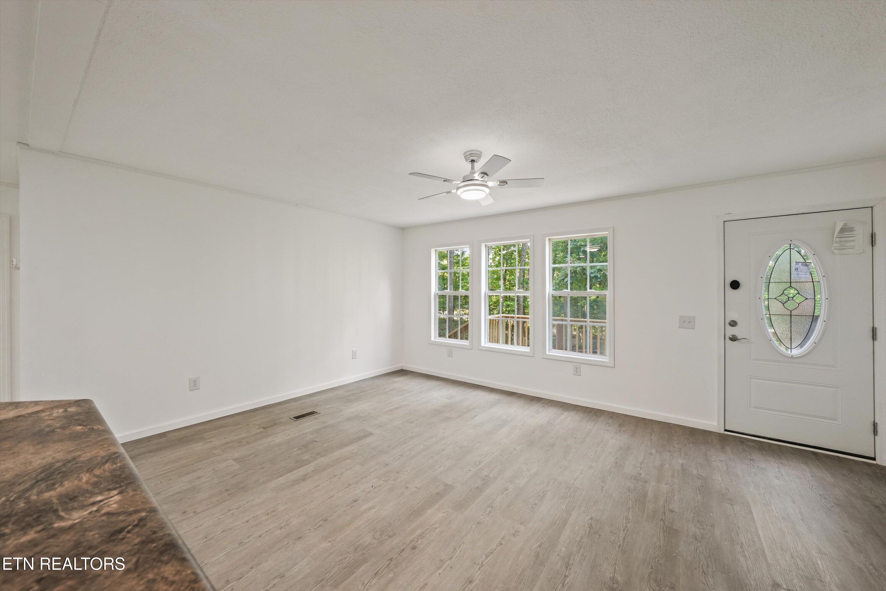 Vacant room with gray wood-look floors, three windows, and a front door with an oval glass insert.