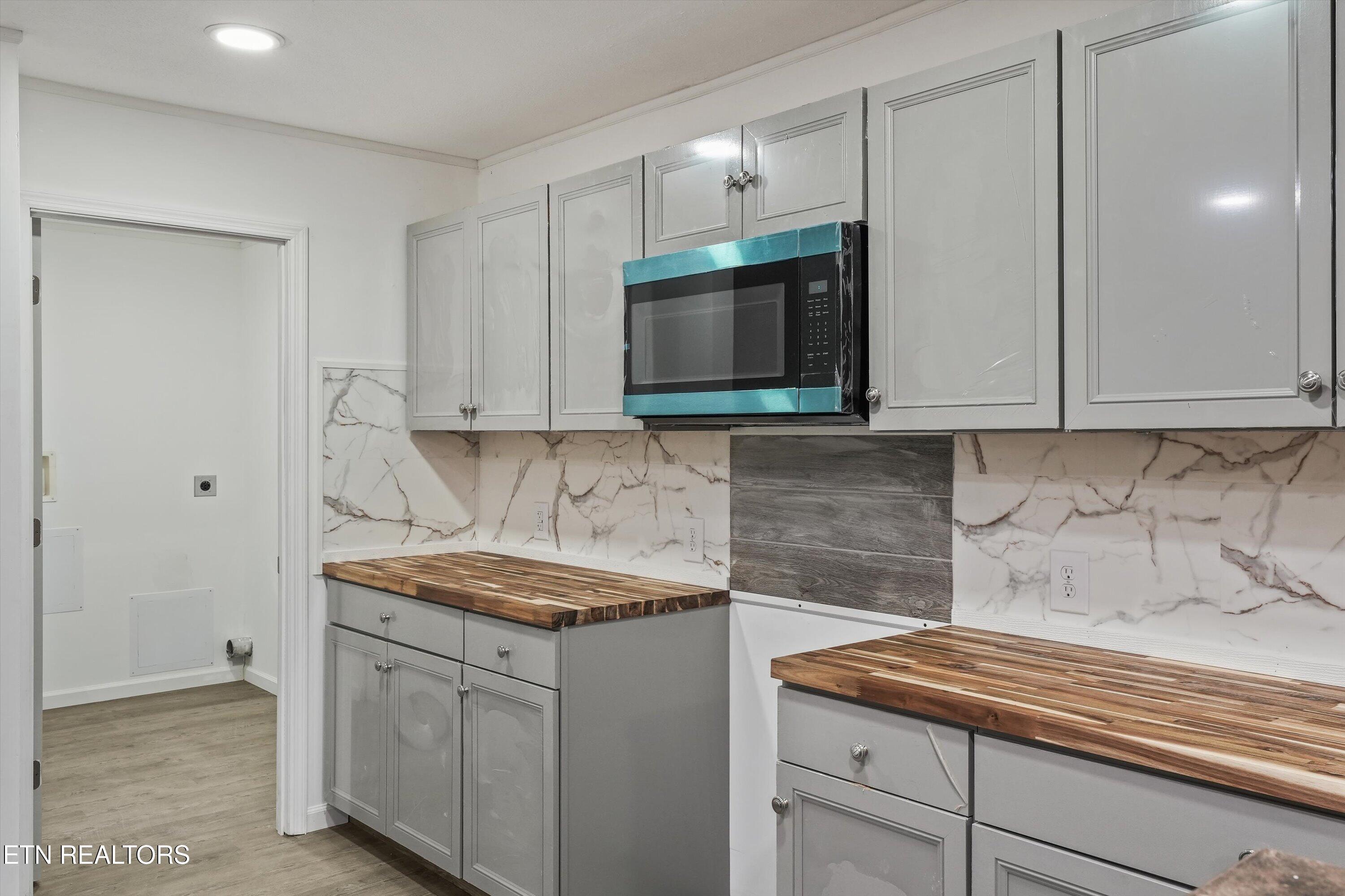 Kitchen with gray cabinets, butcher-block countertops, marble-look backsplash, and a built-in microwave.