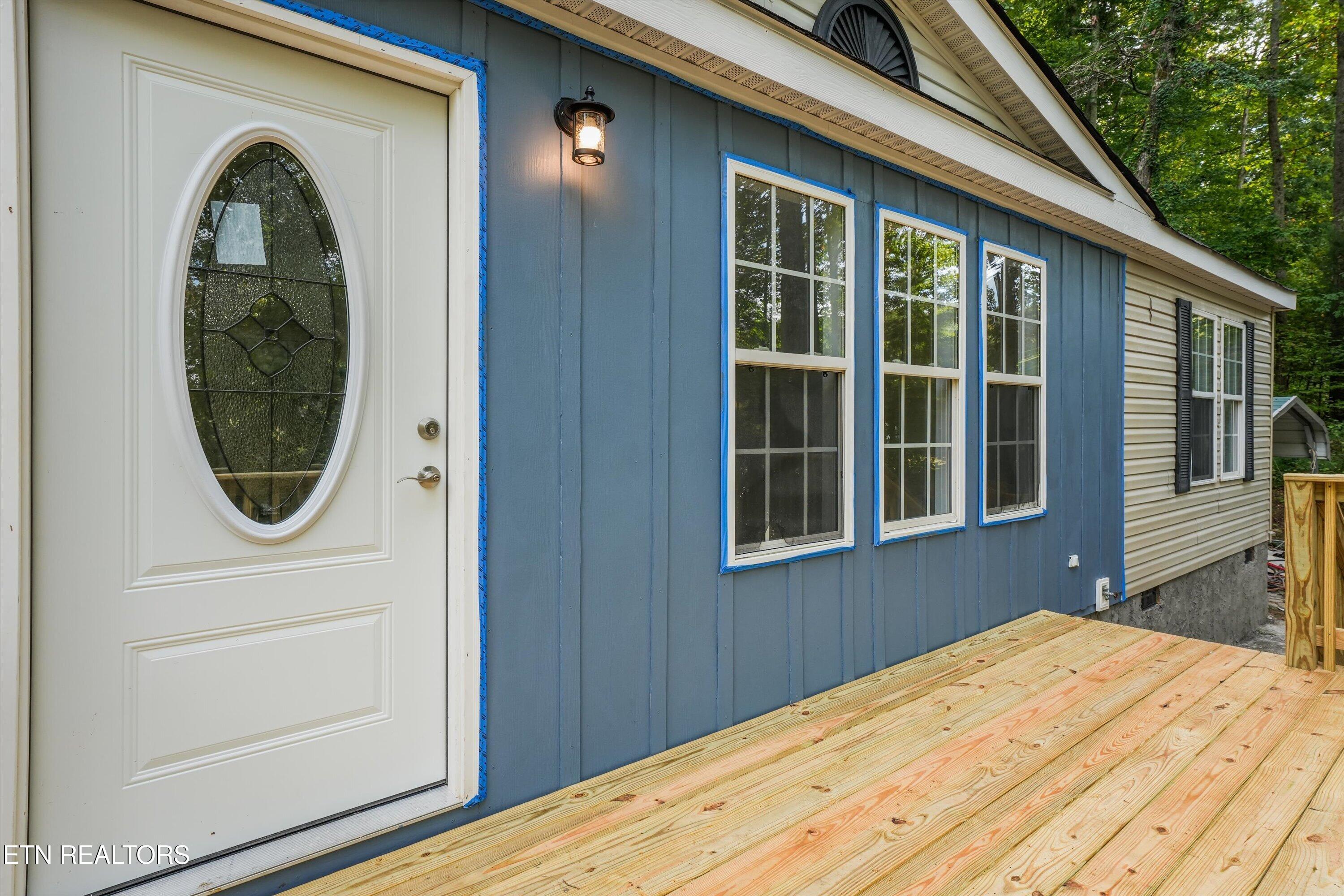Blue-sided home exterior with an oval-glass entry door and a new wooden deck.