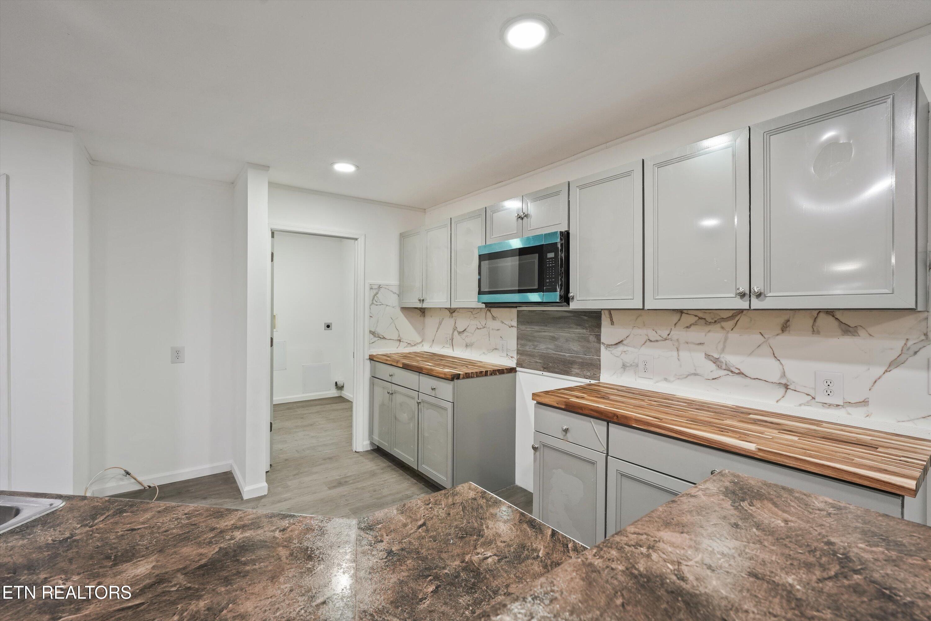 Kitchen with gray cabinets, butcher-block counters, marble-look backsplash, and built-in microwave.