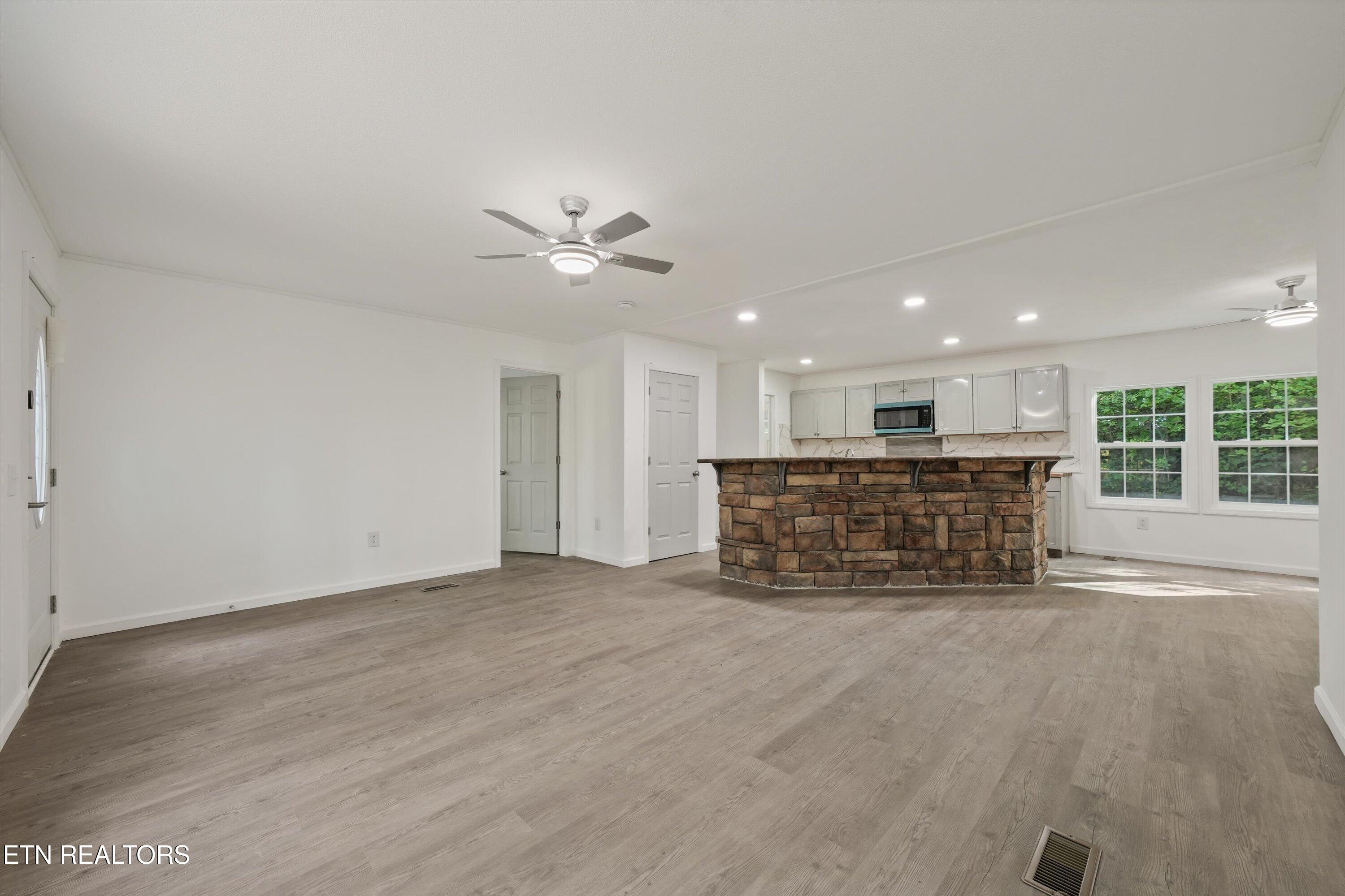 Vacant open-plan kitchen and living area with a curved stone breakfast bar and gray plank flooring.