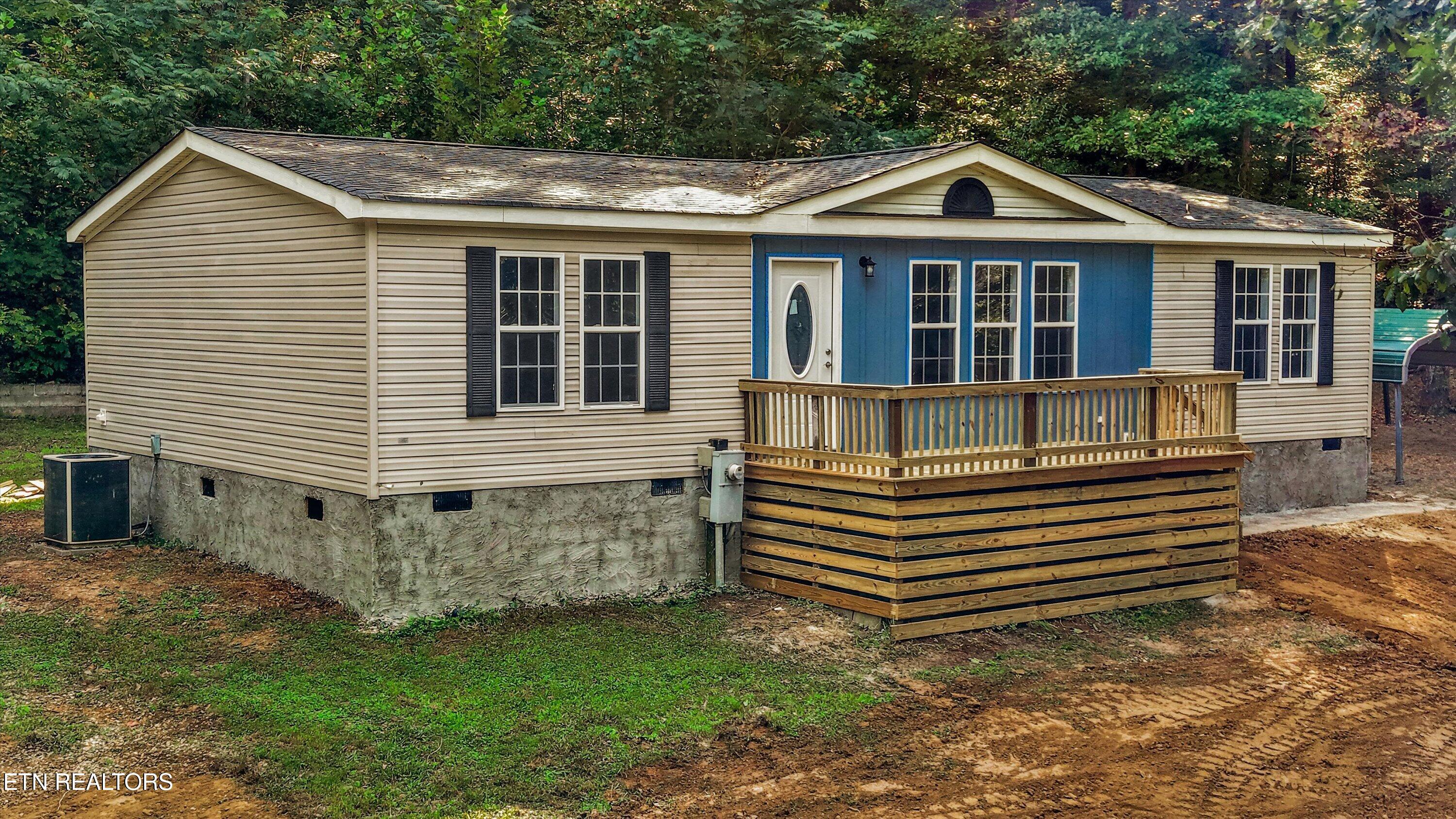 Beige home with blue entry siding and a raised wooden deck surrounded by trees.