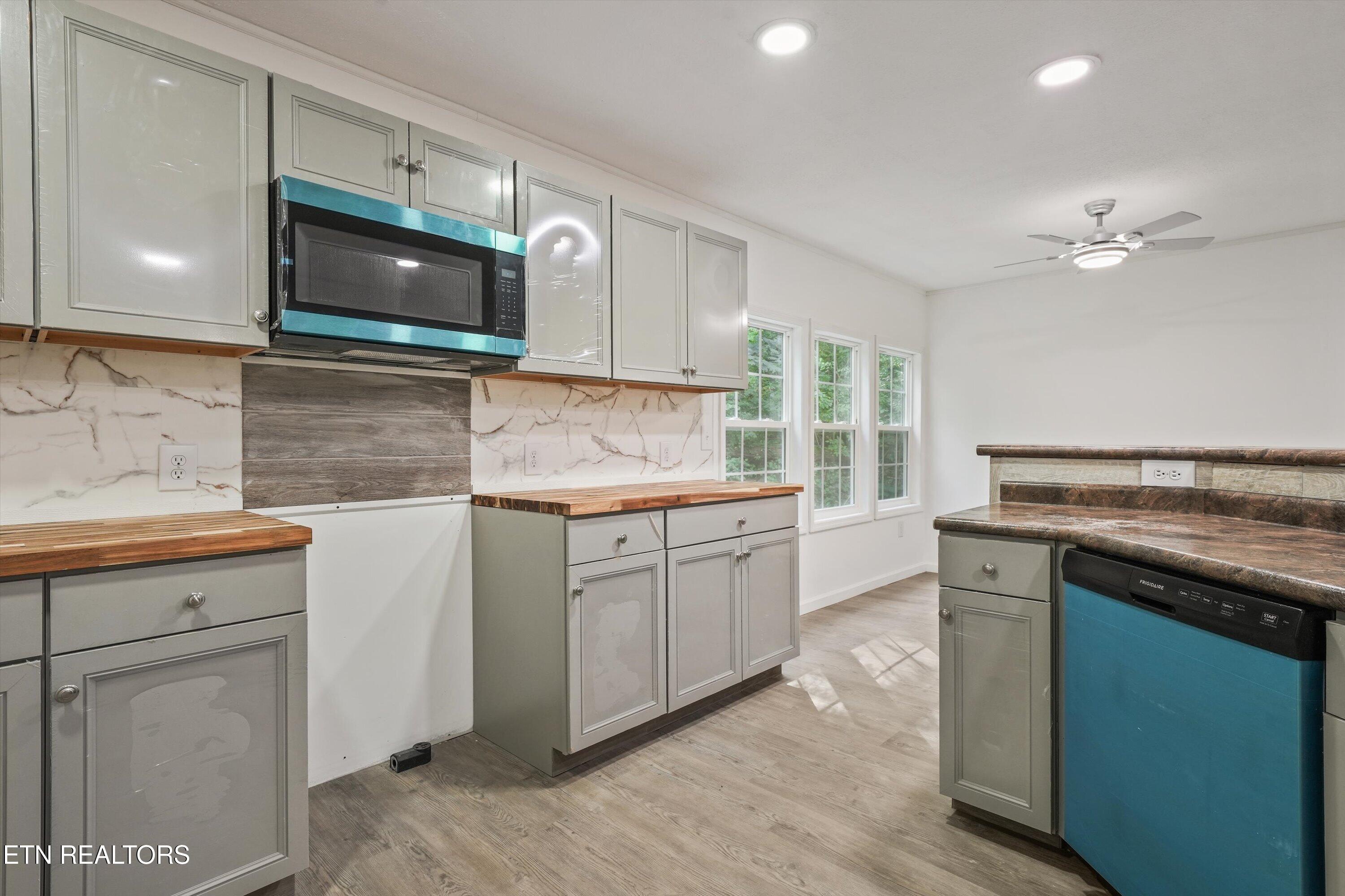 Kitchen with gray cabinets, butcher-block counters, marble-look backsplash, and a blue-front dishwasher.