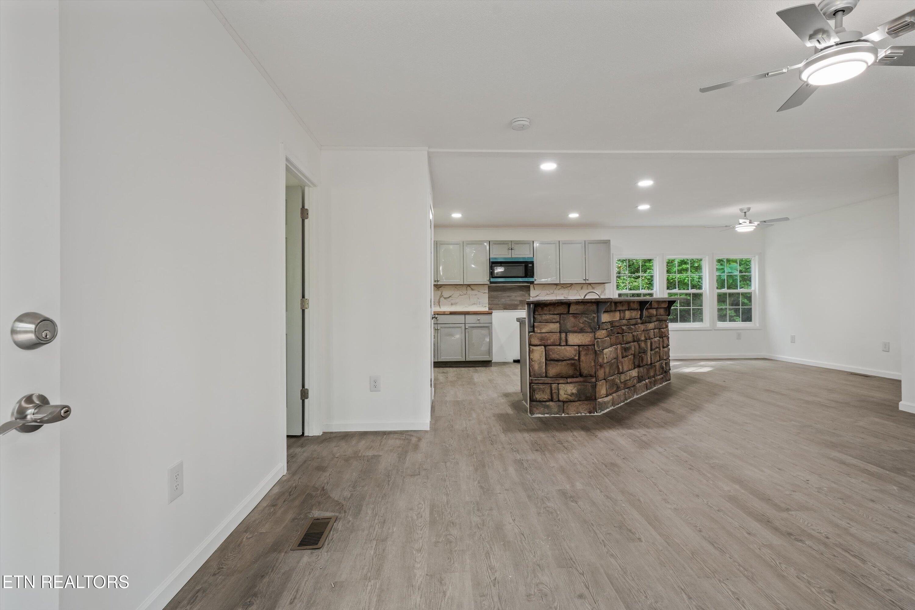 Open-plan kitchen and living area with a prominent stone-faced island and gray wood-look flooring.