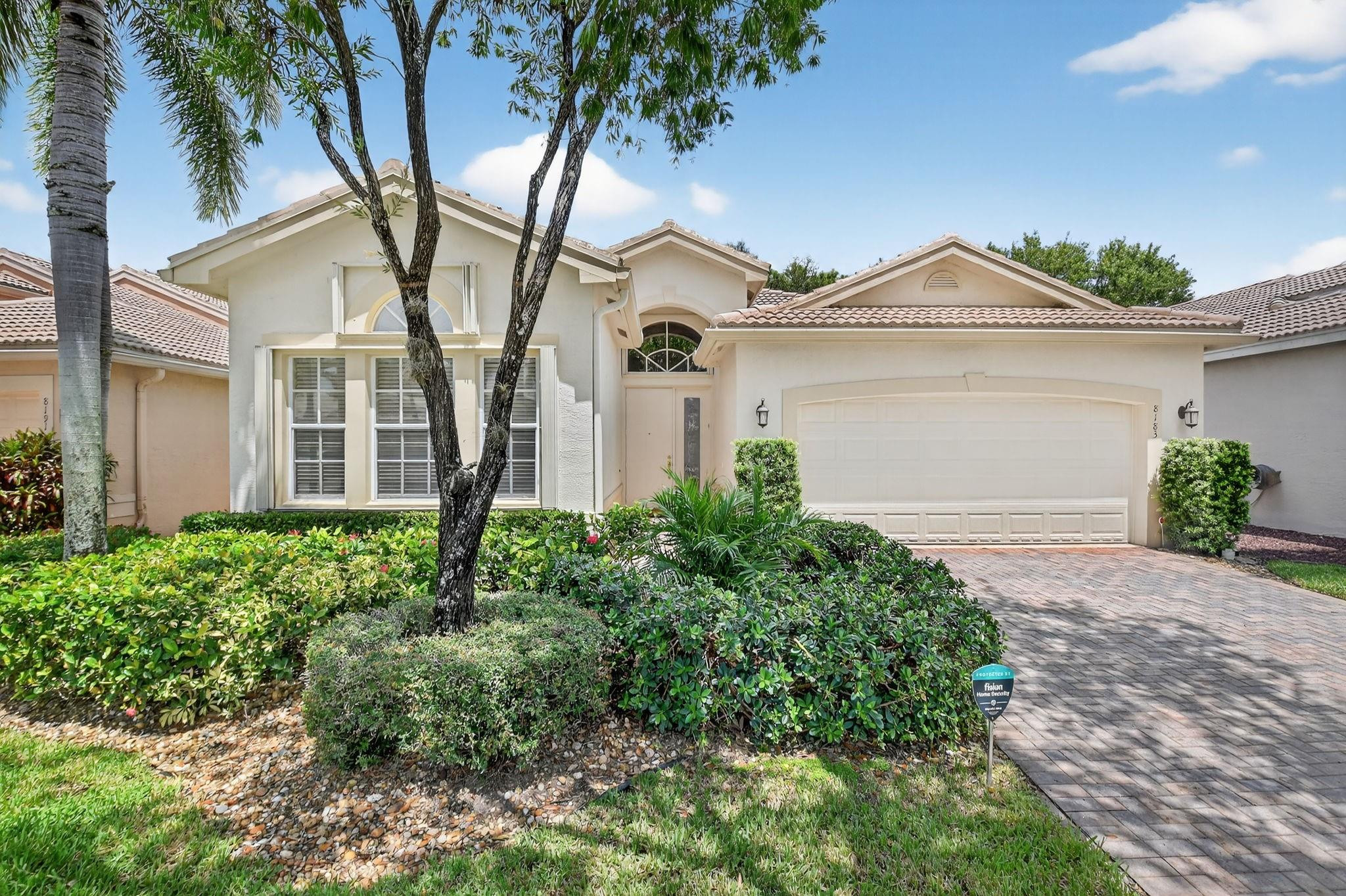 Florida home with a tiled roof, two-car garage, paver driveway, and tropical landscaping.