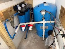 Two blue water system tanks connected by white plumbing and valves in a utility area.