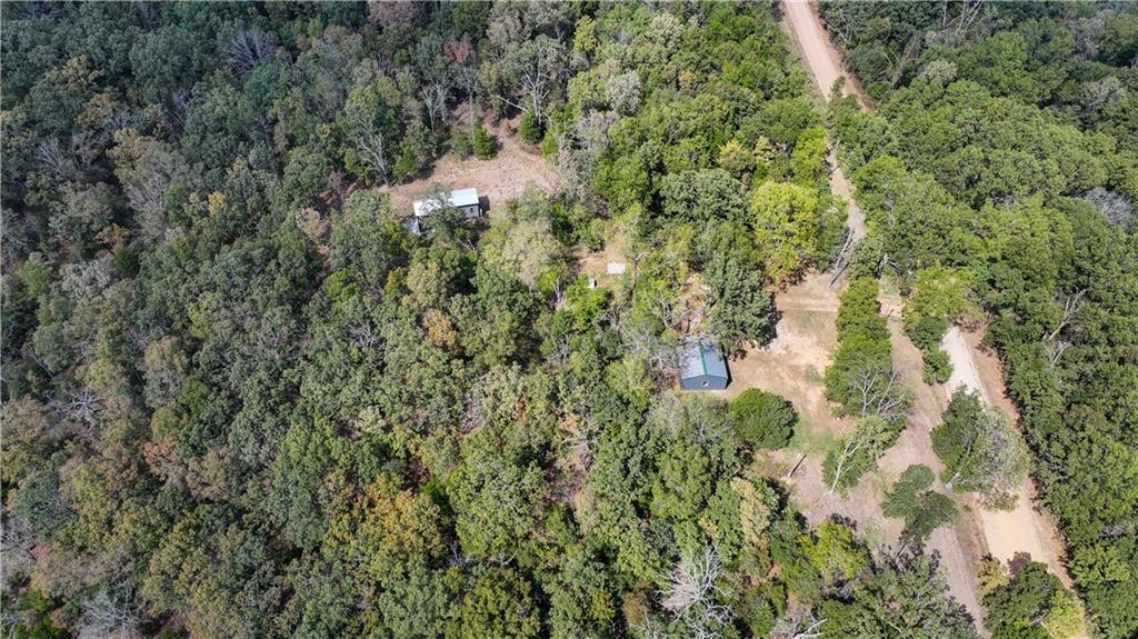 Aerial view of wooded property with a dirt road, clearing, and two small buildings.