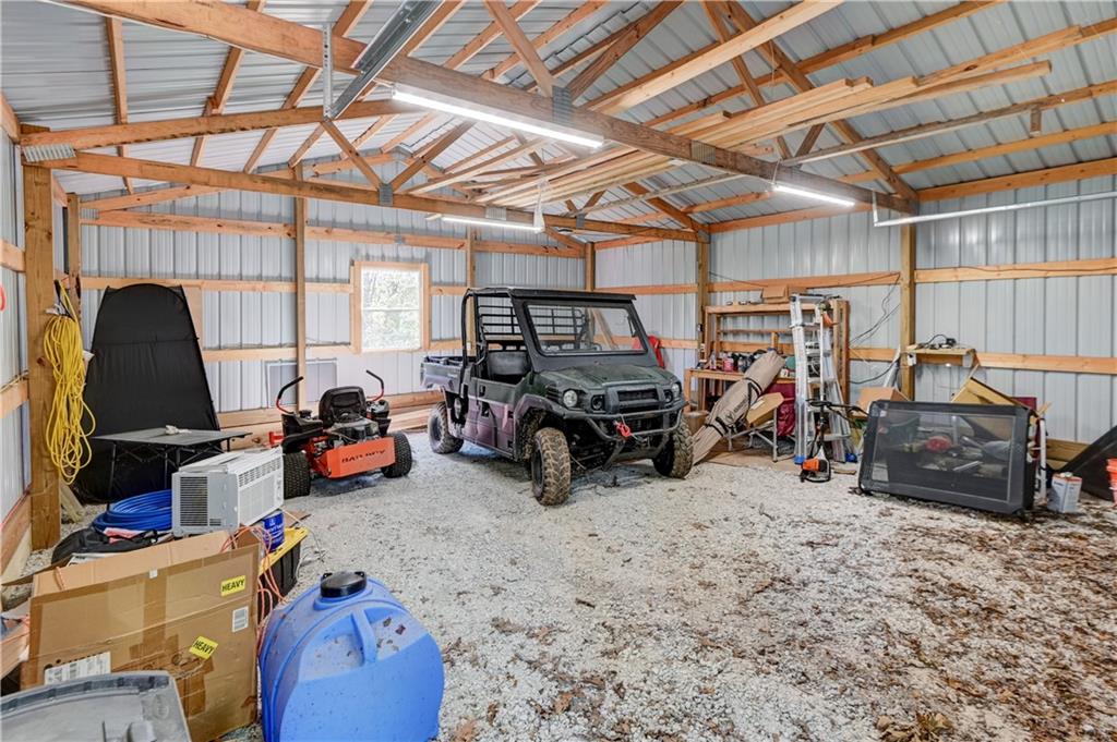 Workshop with exposed roof trusses, gravel floor, and a utility terrain vehicle.