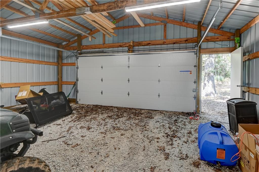 Pole-barn garage with gravel floor, exposed wooden trusses, and a large overhead door.