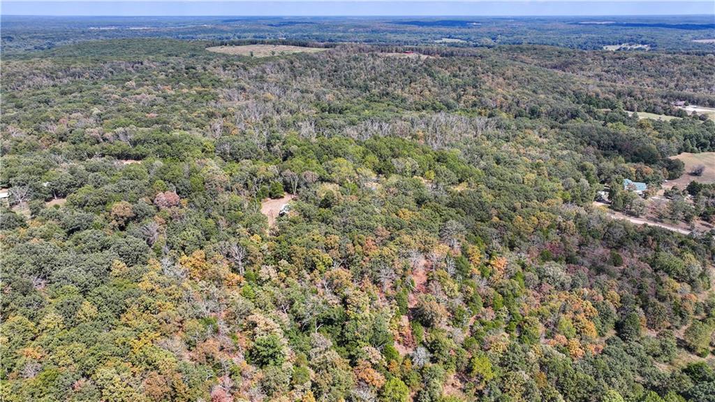 Aerial view of rolling wooded land with scattered clearings and autumn-colored foliage.