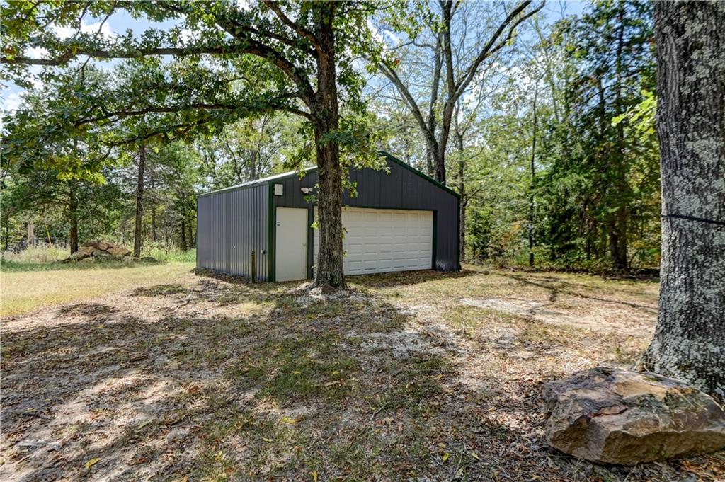 Detached dark metal garage with white overhead door in a wooded clearing.