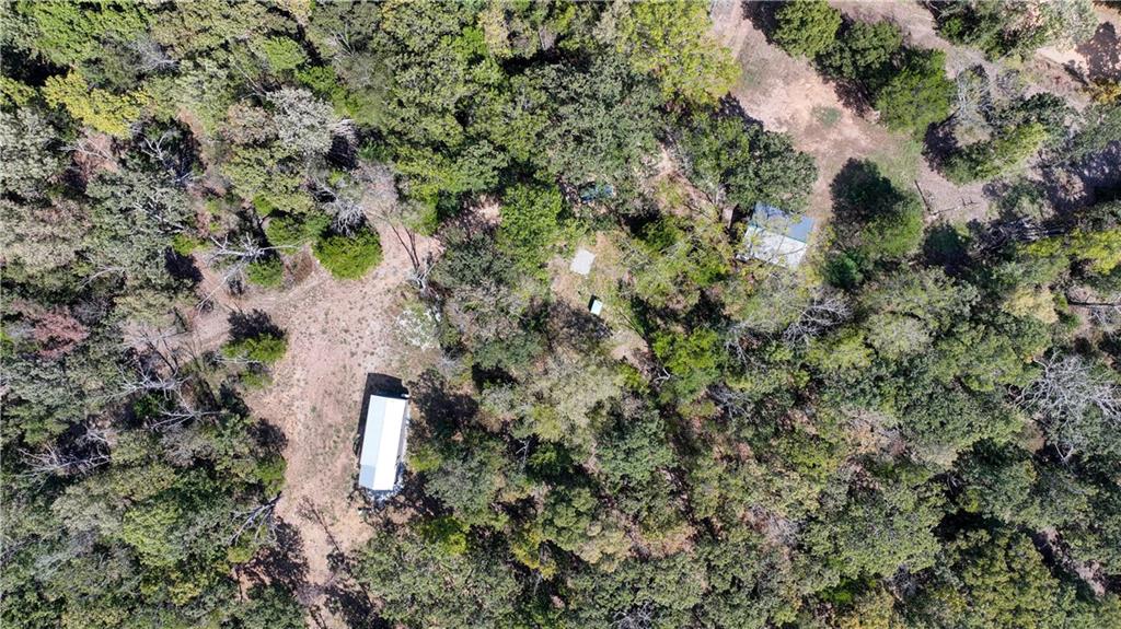 Aerial view of wooded property with a long white-roofed structure and scattered clearings.